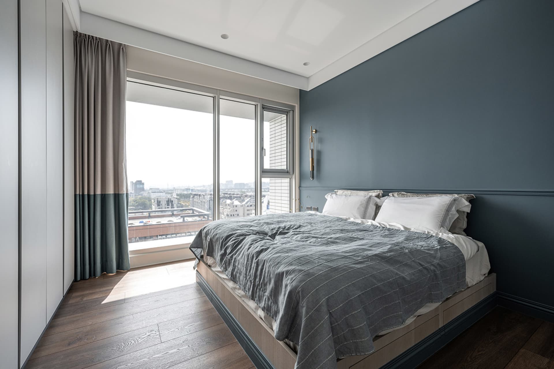 A cozy modern bedroom with a bed, fabric window curtains, and a view of the city.