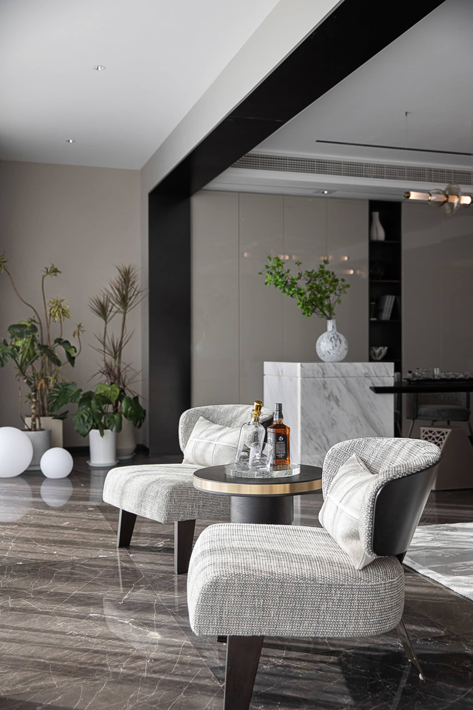 Modern living room with marble floor, grey upholstered chairs, and a round side table with drinks.