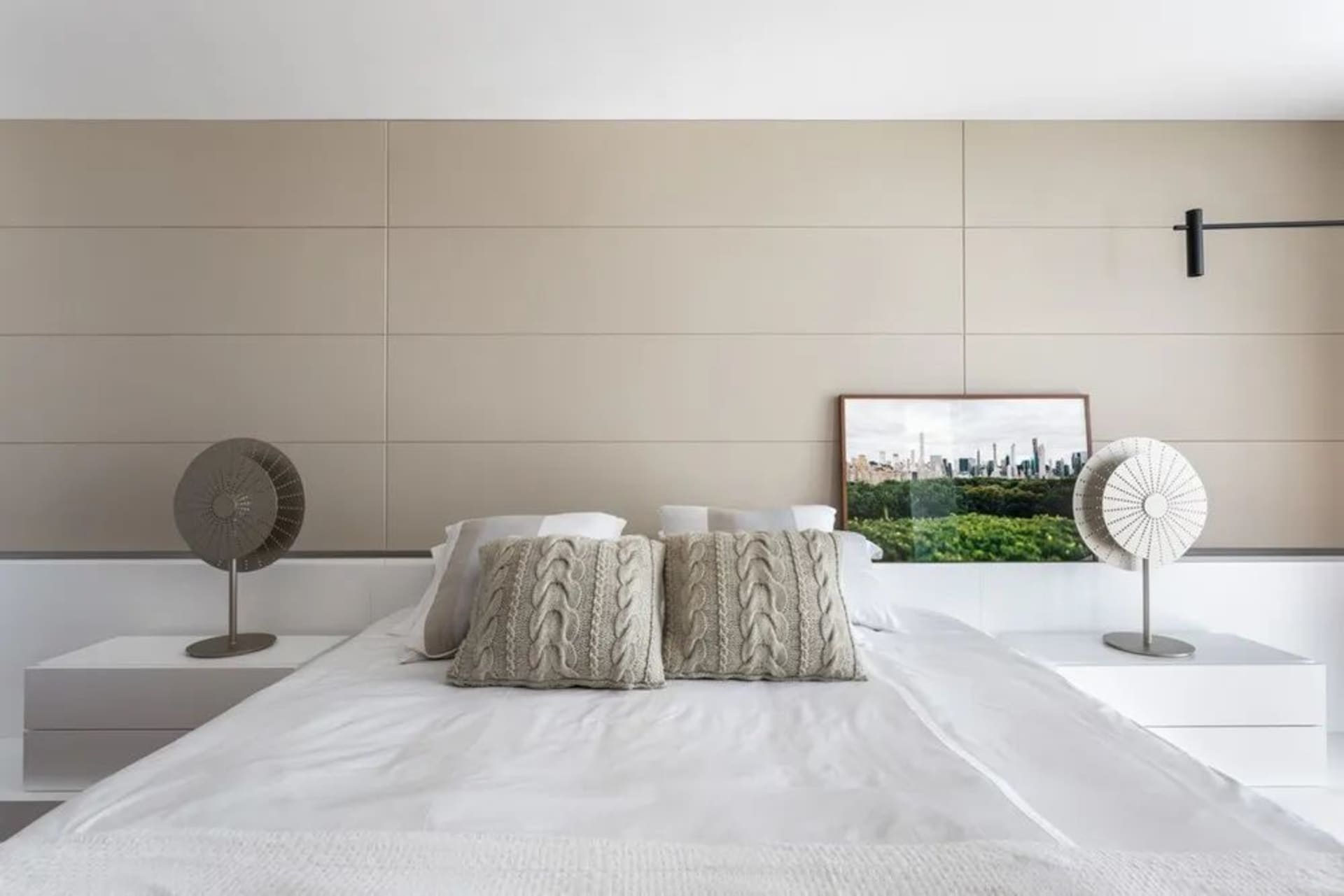 A modern, minimalist bedroom with a white bed, beige wall paneling, and decorative pillows.