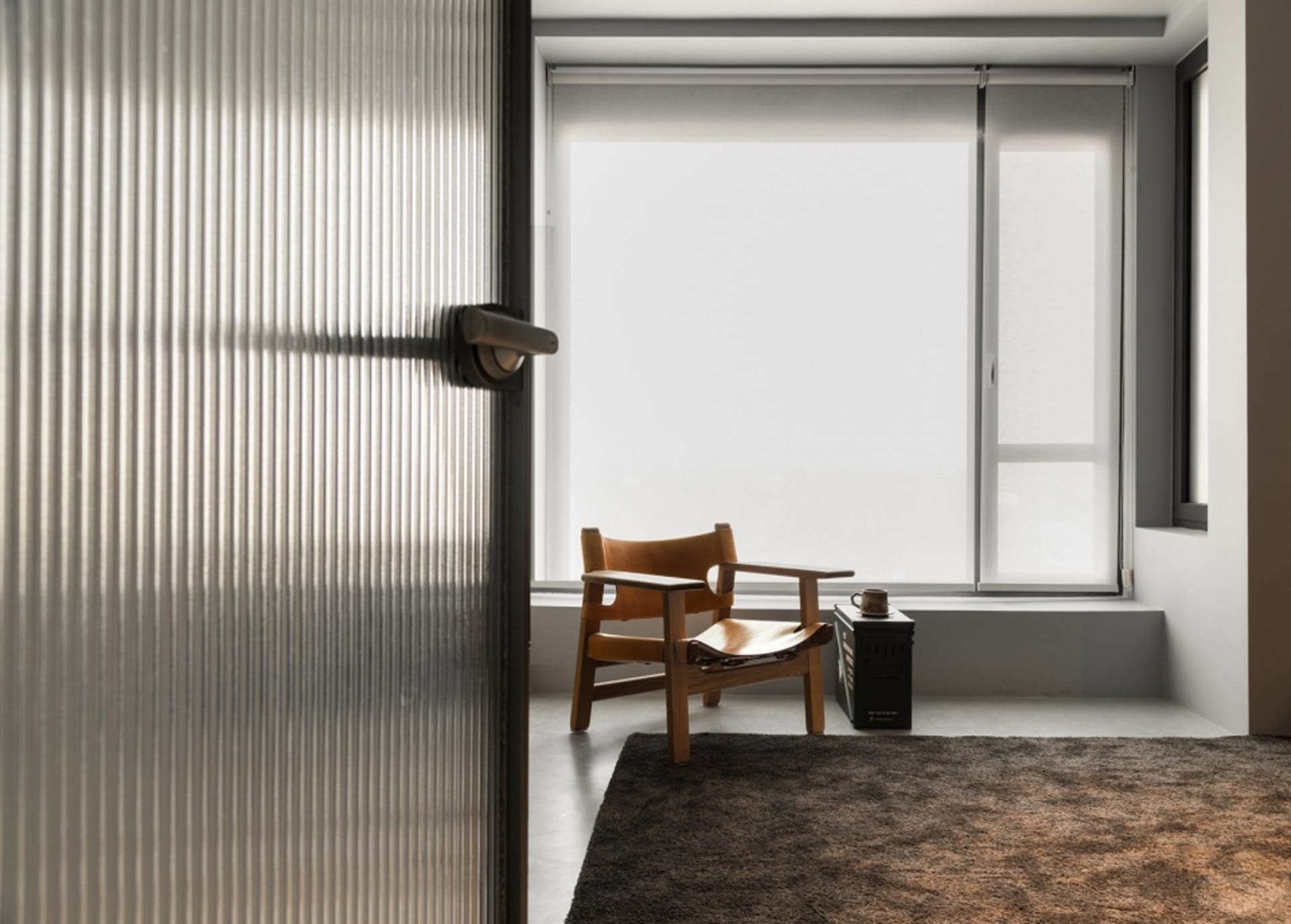 A modern minimalist living room with a wooden chair, glass window, and carpeted floor.