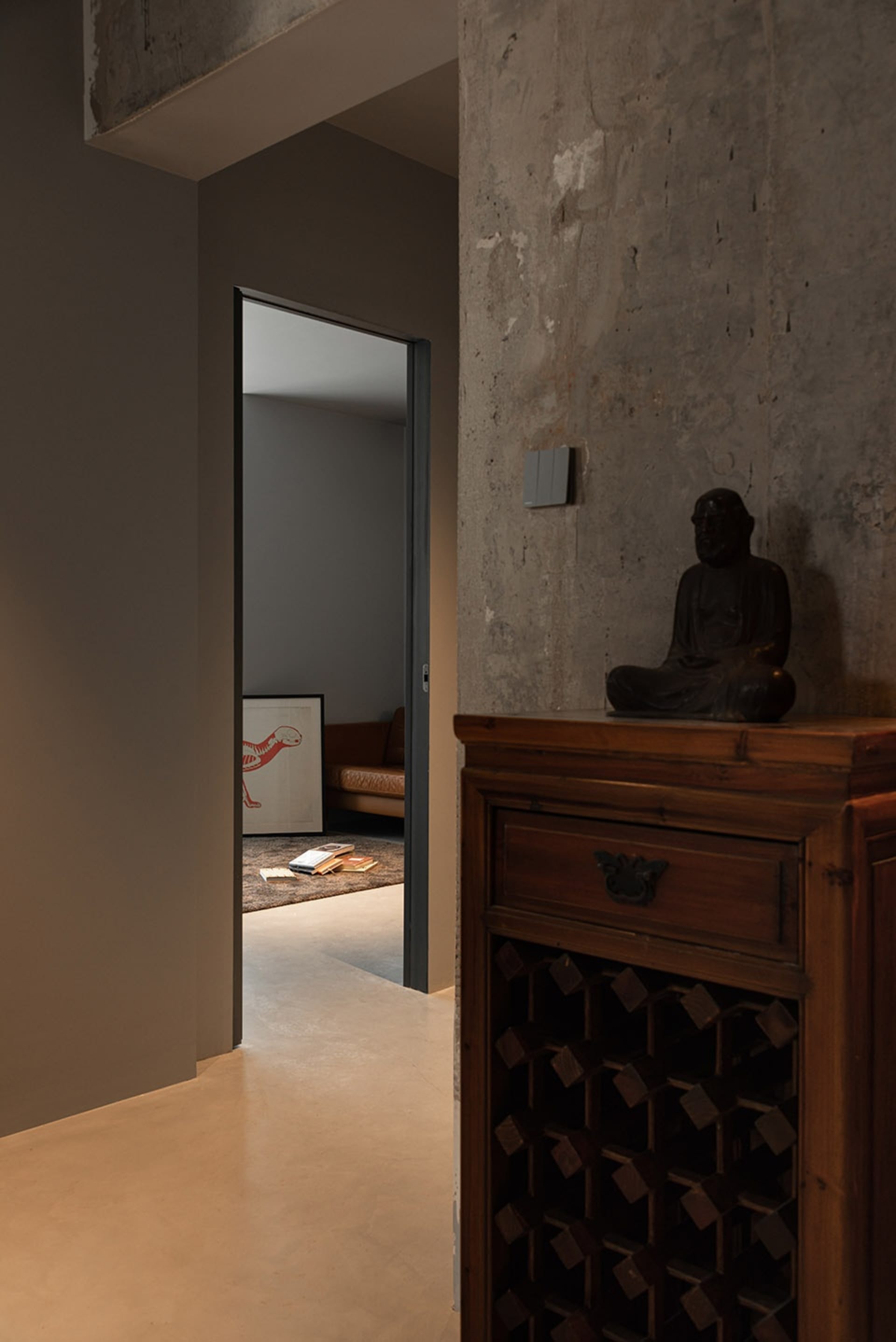 A hallway with a concrete floor, exposed concrete walls, and a wooden cabinet with a Buddha statue and a book.