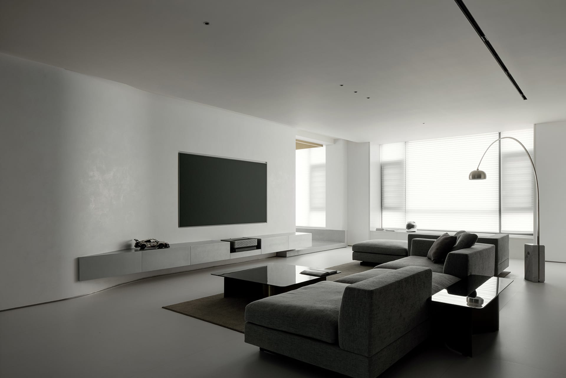 Minimalist living room with concrete walls and a black leather sofa, featuring a sleek black coffee table, large windows, and