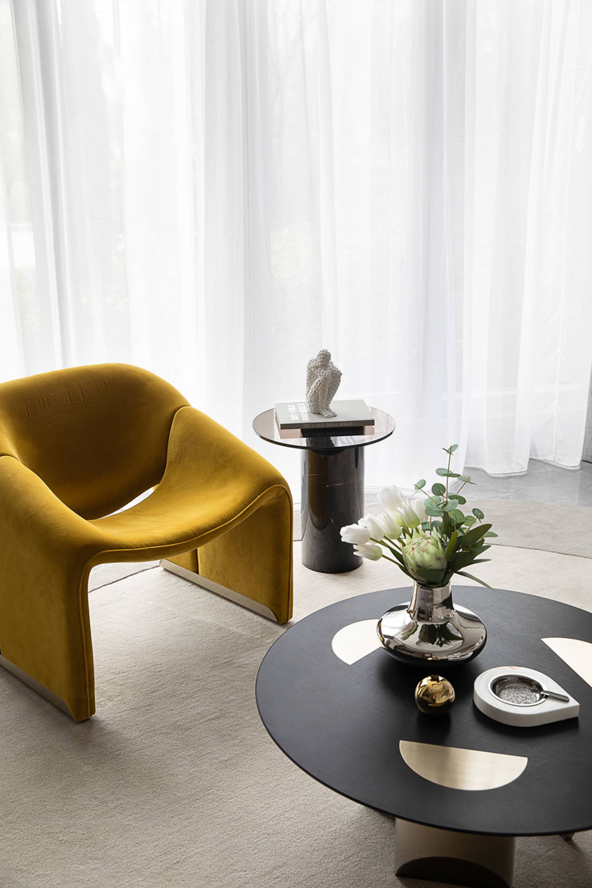 Modern living room featuring a yellow velvet armchair, a round coffee table with a vase of flowers and a metallic ashtray, an
