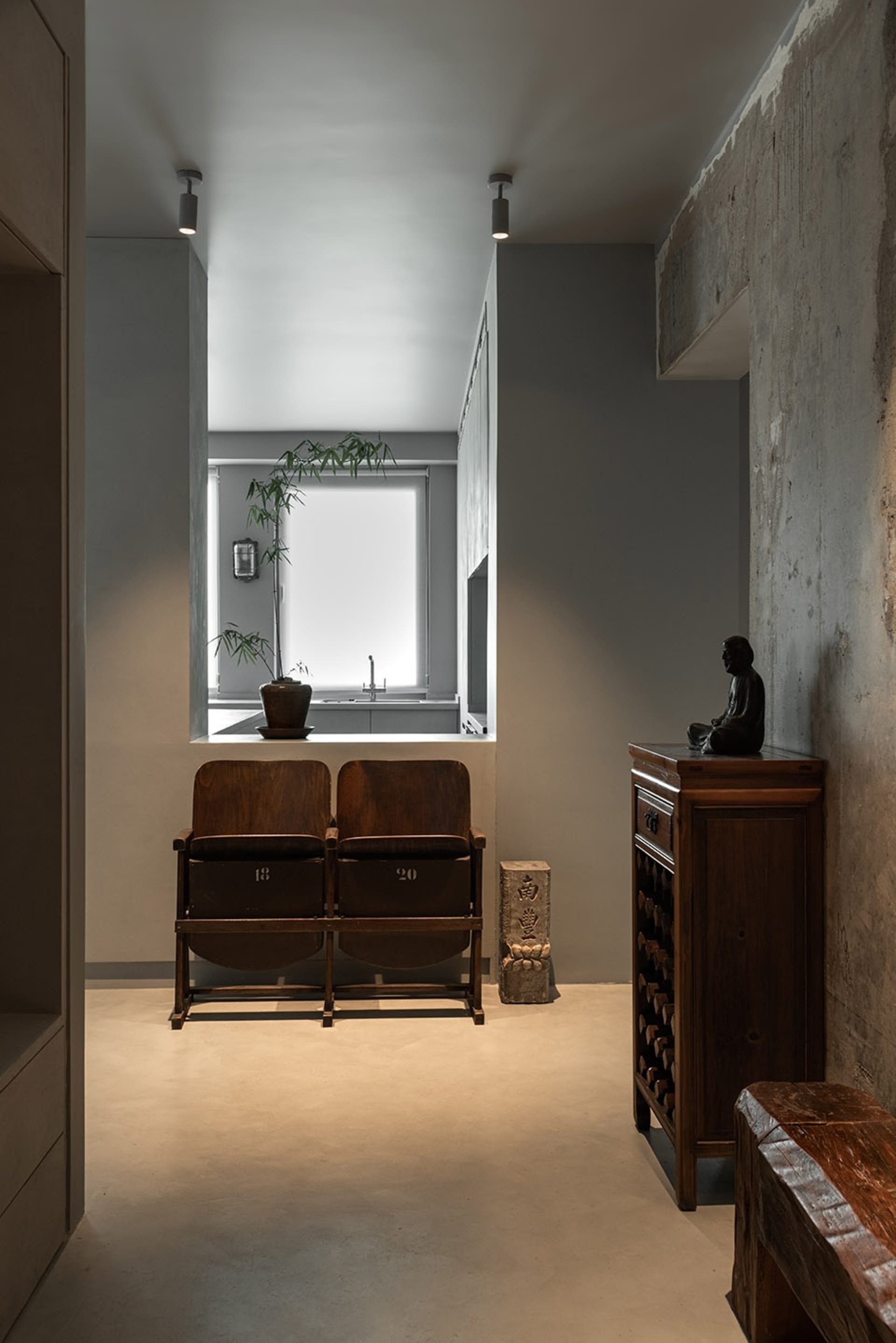 A minimalist living room featuring wooden chairs, concrete walls, and glass panels.