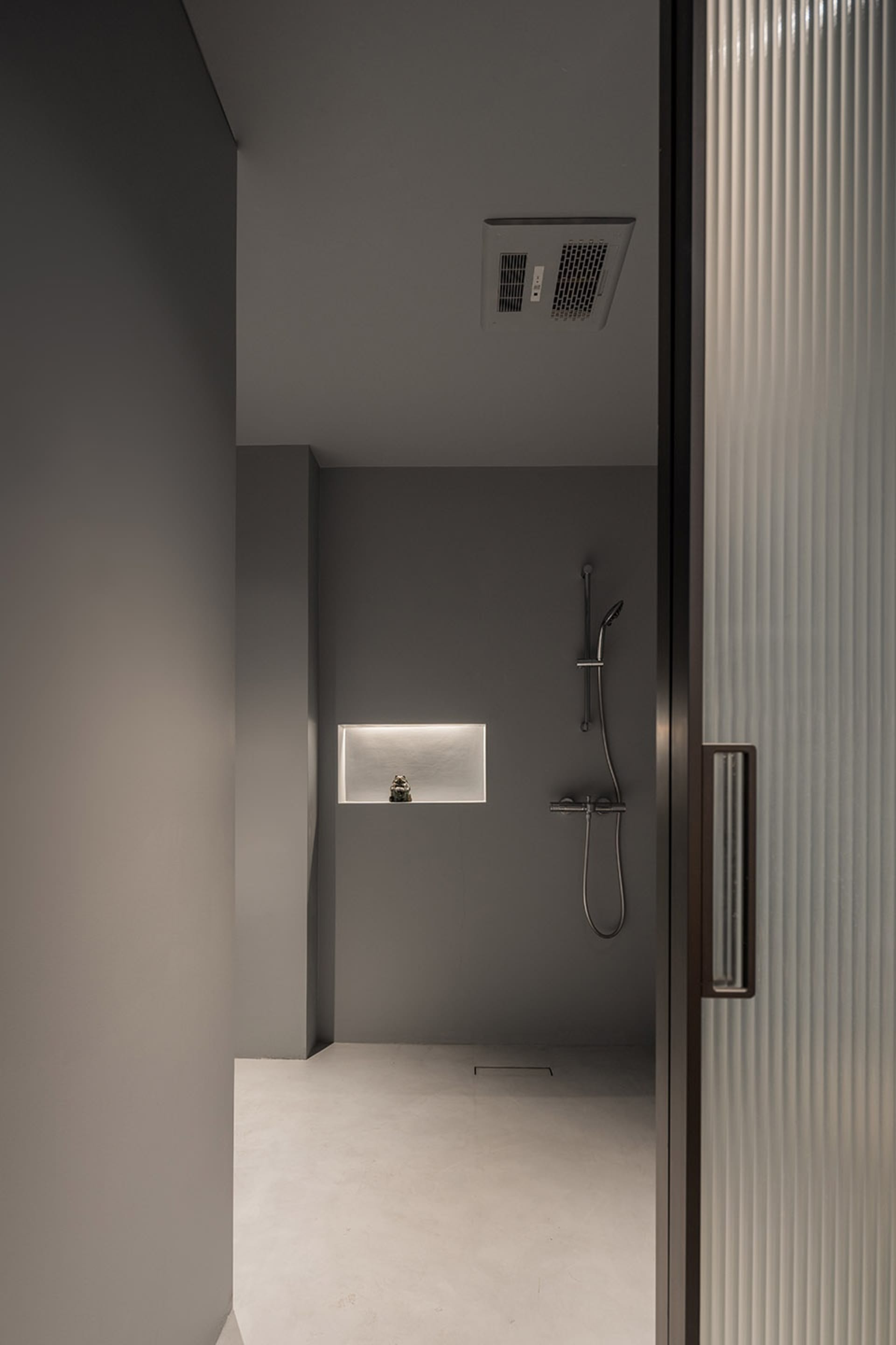 A modern minimalist bathroom with a concrete floor and walls, featuring a shower with a minimalist design.