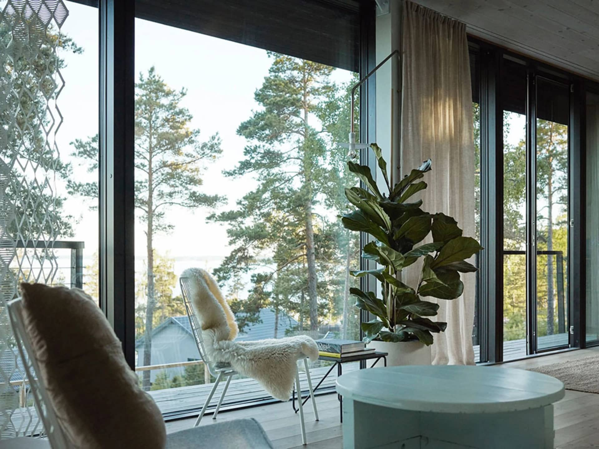 A minimalist living room featuring large glass windows overlooking a forested area.