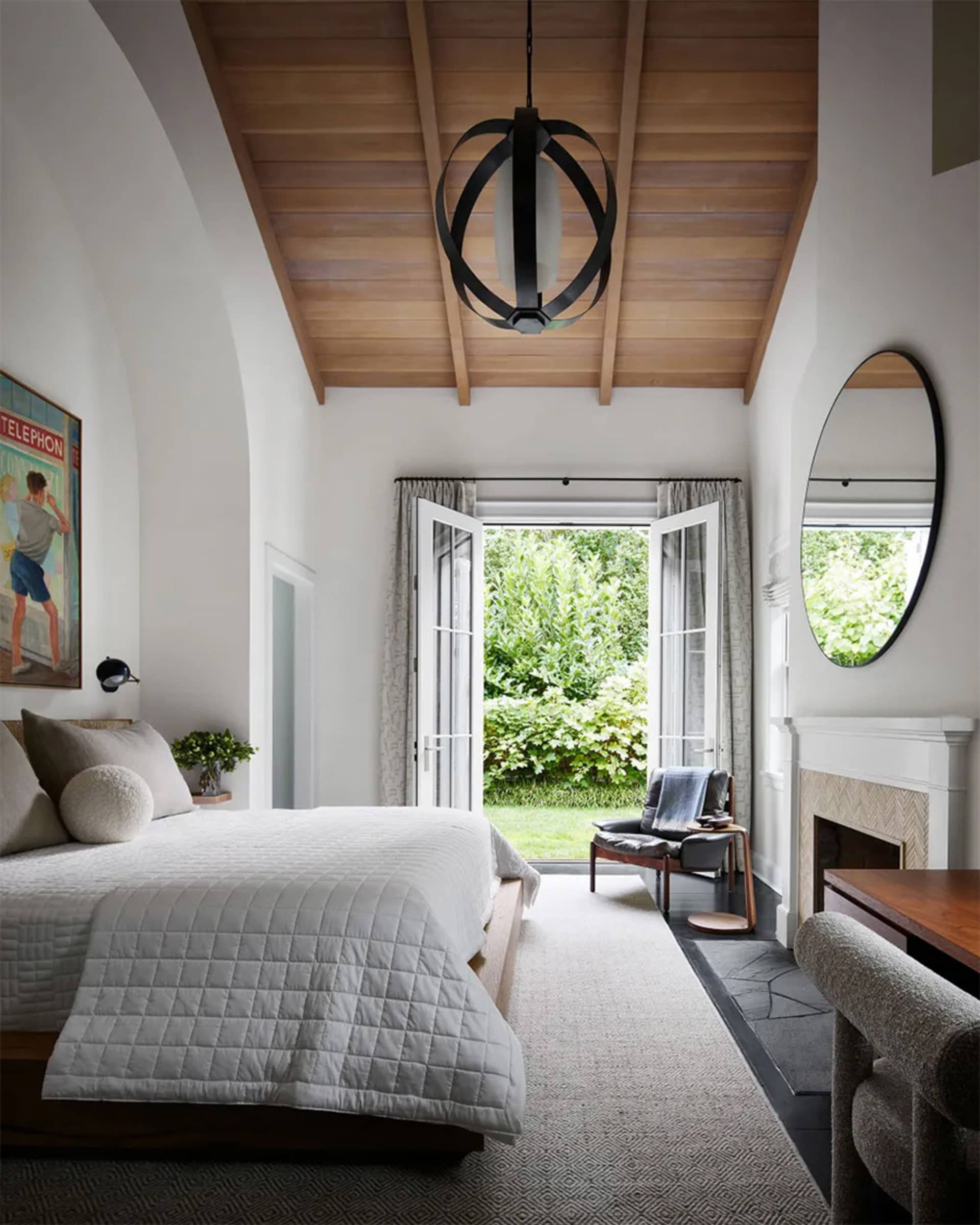 A modern bedroom with white painted walls, wooden flooring, and a large window leading to a garden.