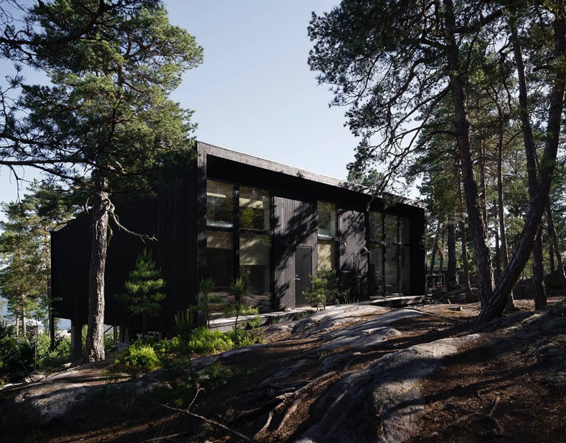 A modern, black wooden house surrounded by trees and rocks.