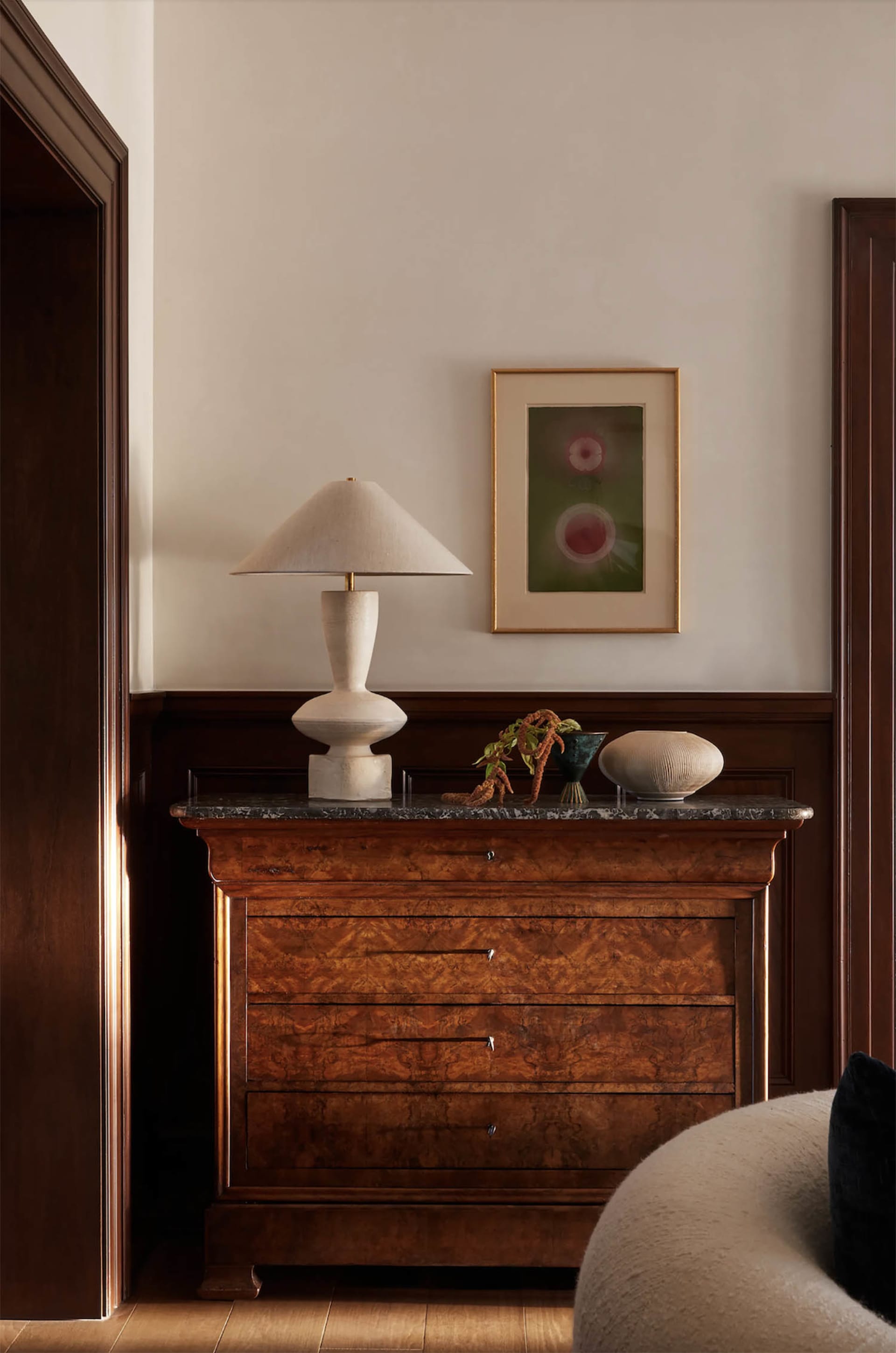 A modern console with a marble top displaying a lamp, vase, and plant.