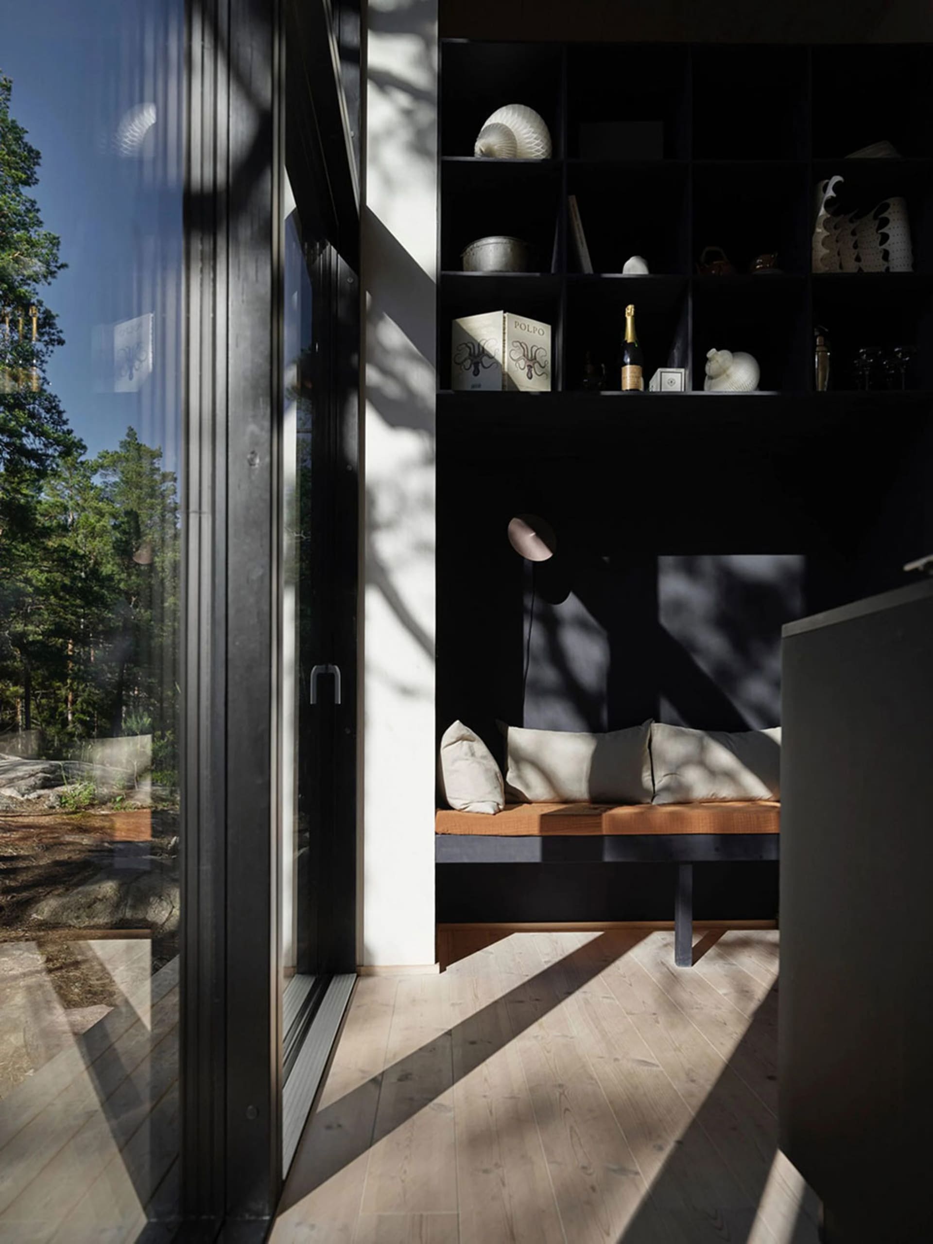 Modern minimalist bedroom with wood and glass materials, featuring a built-in bench seating area and a shelf with decorative
