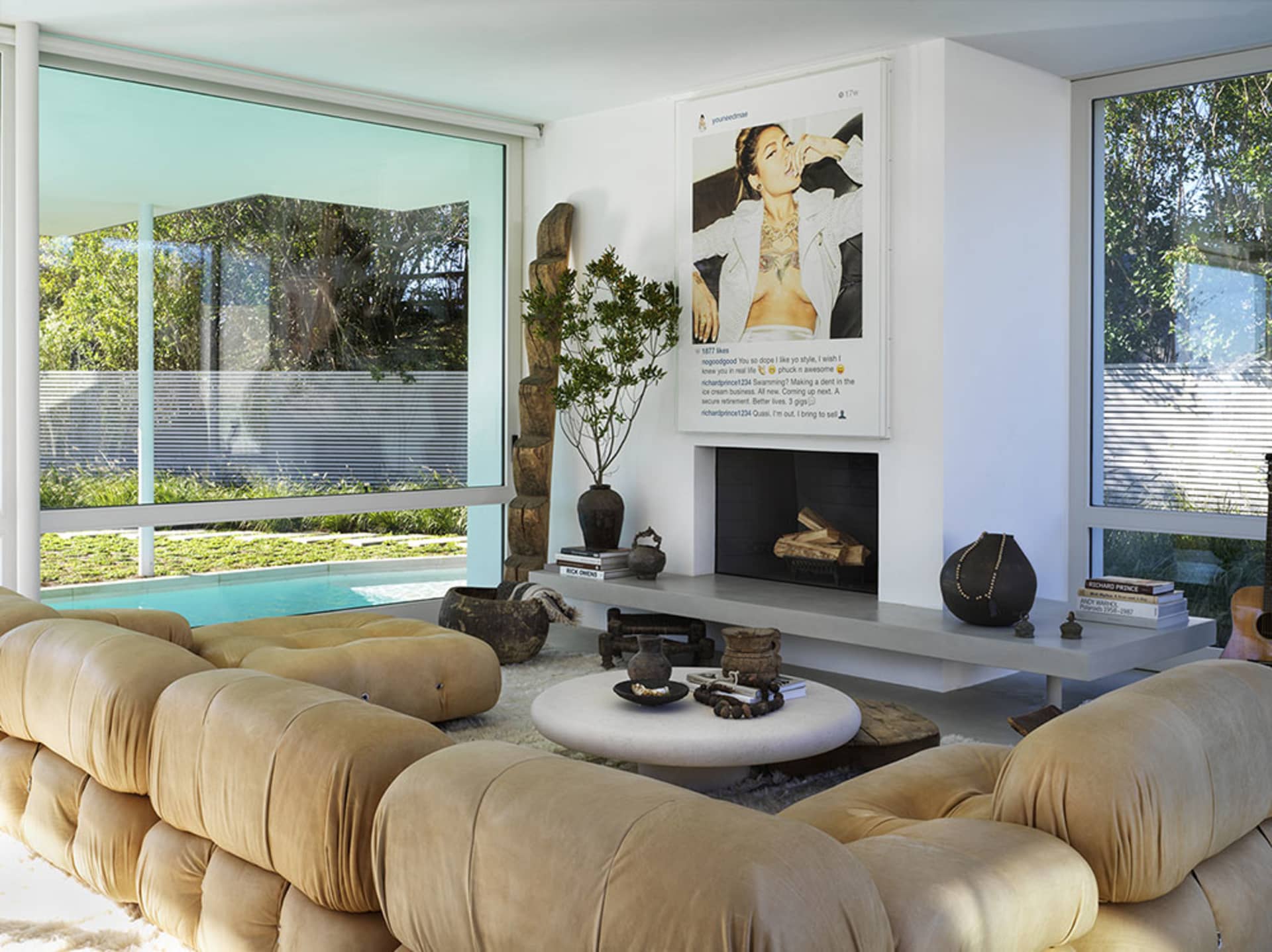 A modern living room with a concrete fireplace, large glass windows overlooking a pool, and a beige sectional sofa.