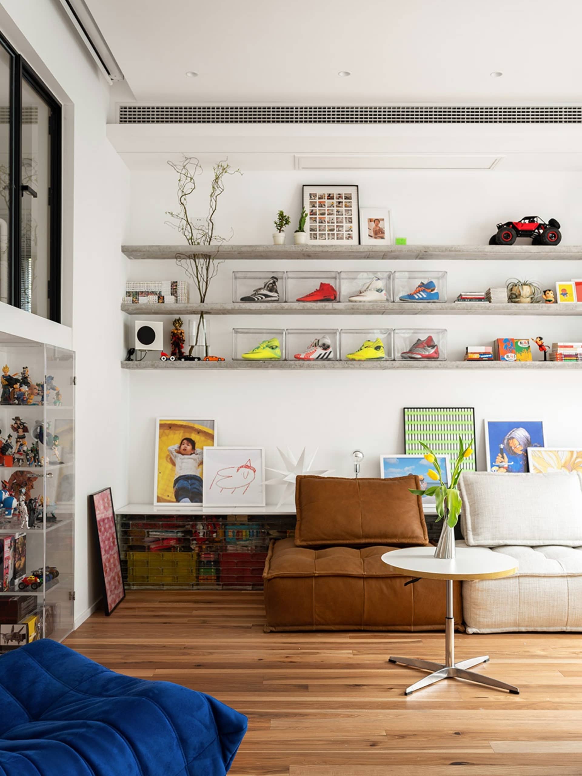 A modern living room with a wooden floor, concrete floating shelves, and a brown leather ottoman.