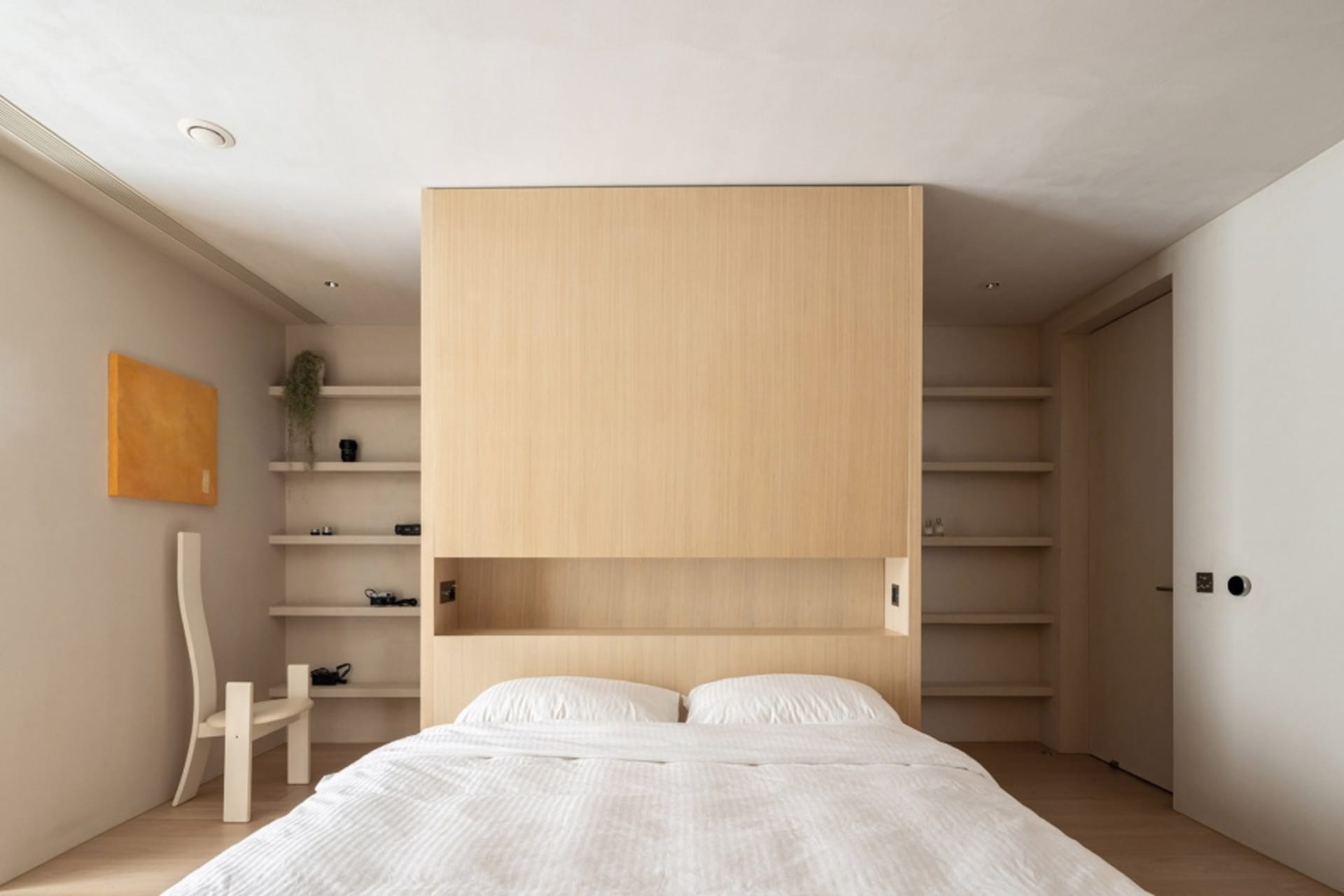 A minimalist bedroom with a wooden wall, white bedding, and floating shelves.