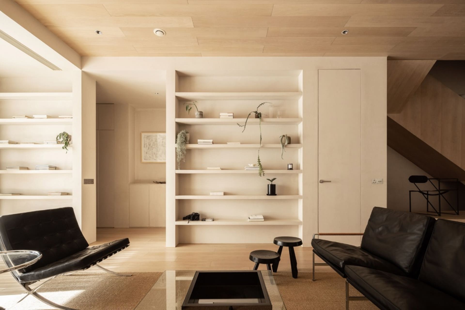 Modern living room with minimalistic design and neutral color palette featuring a black leather sofa, black Barcelona chair,