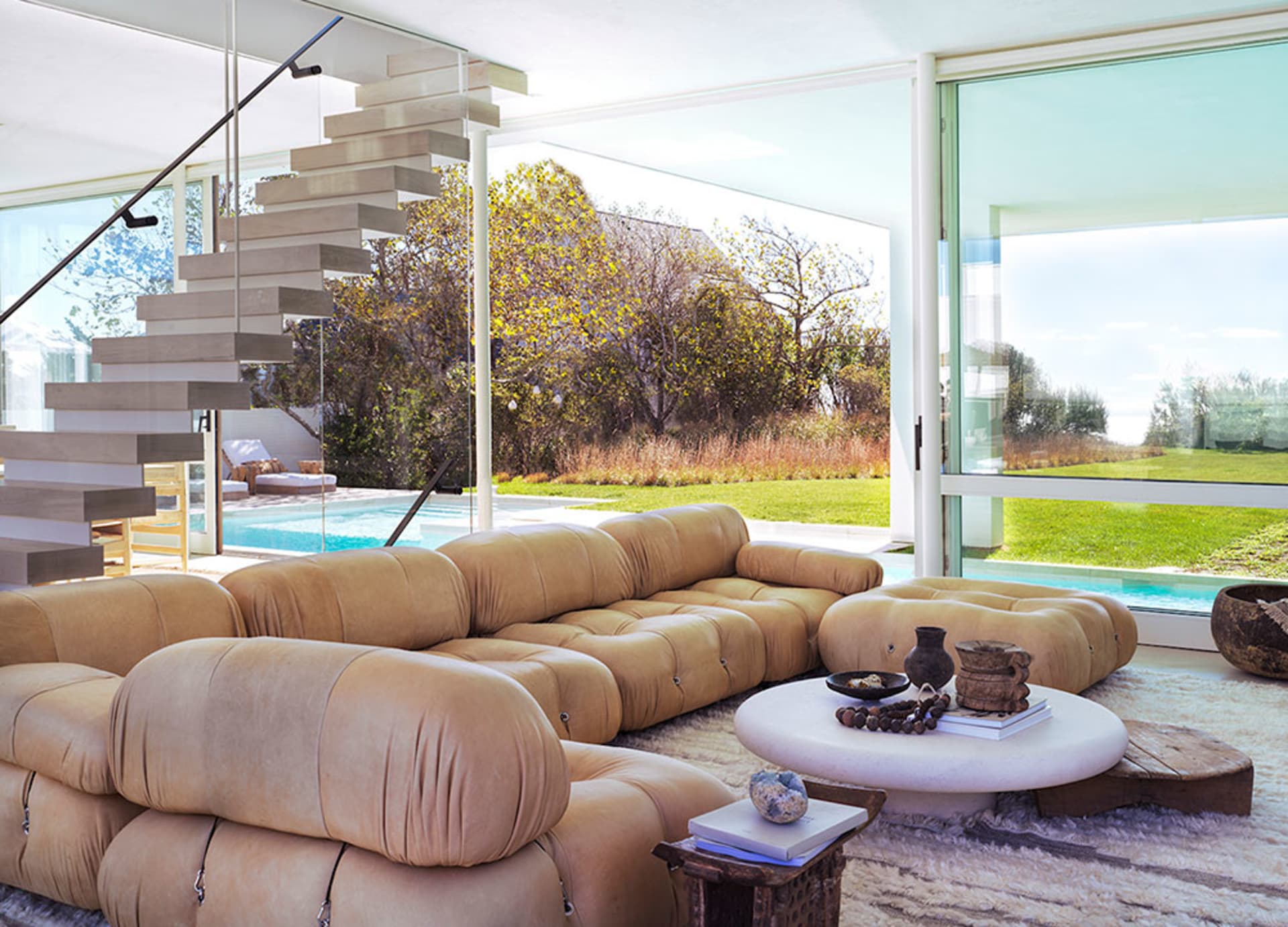 A spacious modern living room featuring comfortable leather furniture, a glass stairway, and a scenic outdoor view.