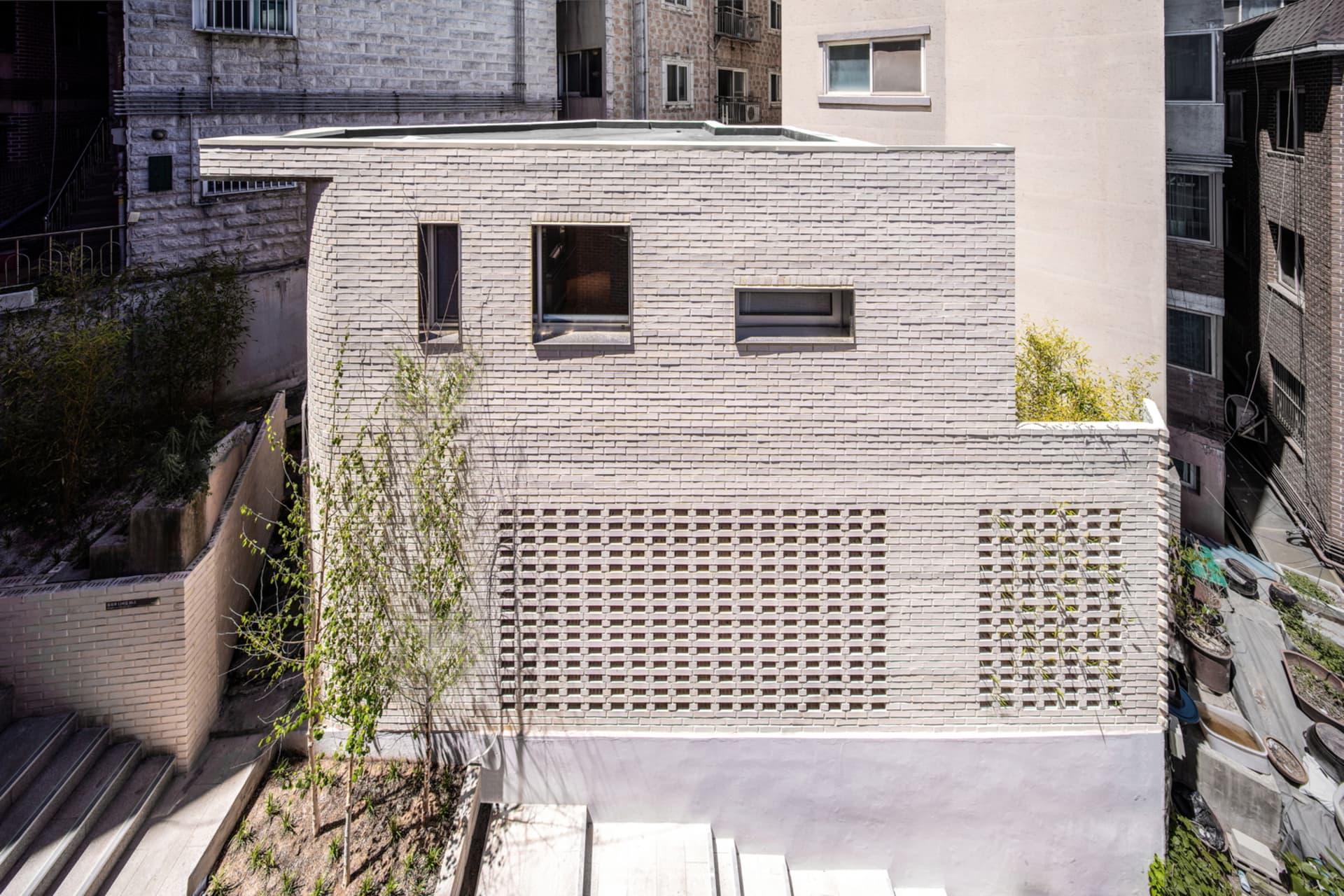 A minimalist building featuring a white brick facade with large glass windows and a green roof garden.