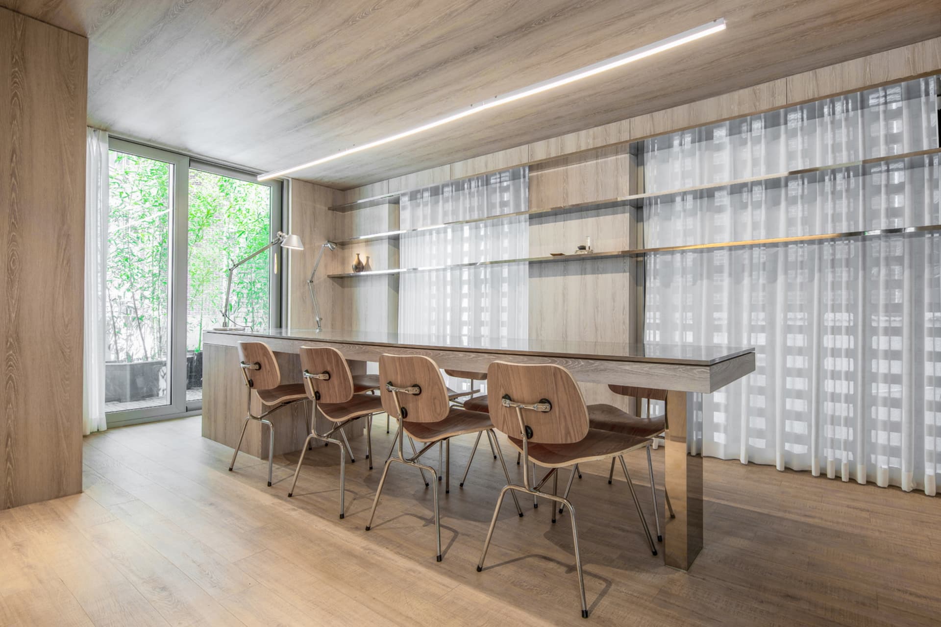 A modern minimalist dining room featuring wooden and metal furniture and white sheer curtains.