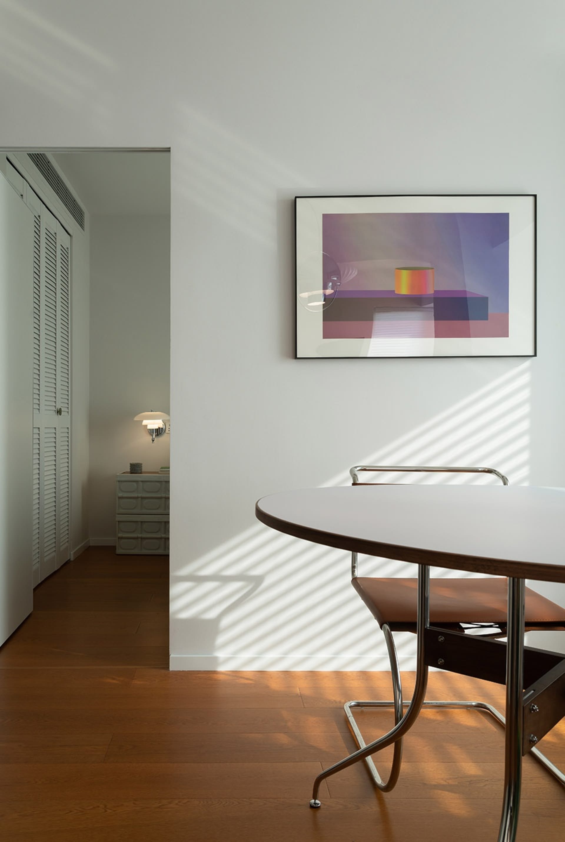 A modern residential room featuring white furniture, a round table, and a framed abstract art piece.