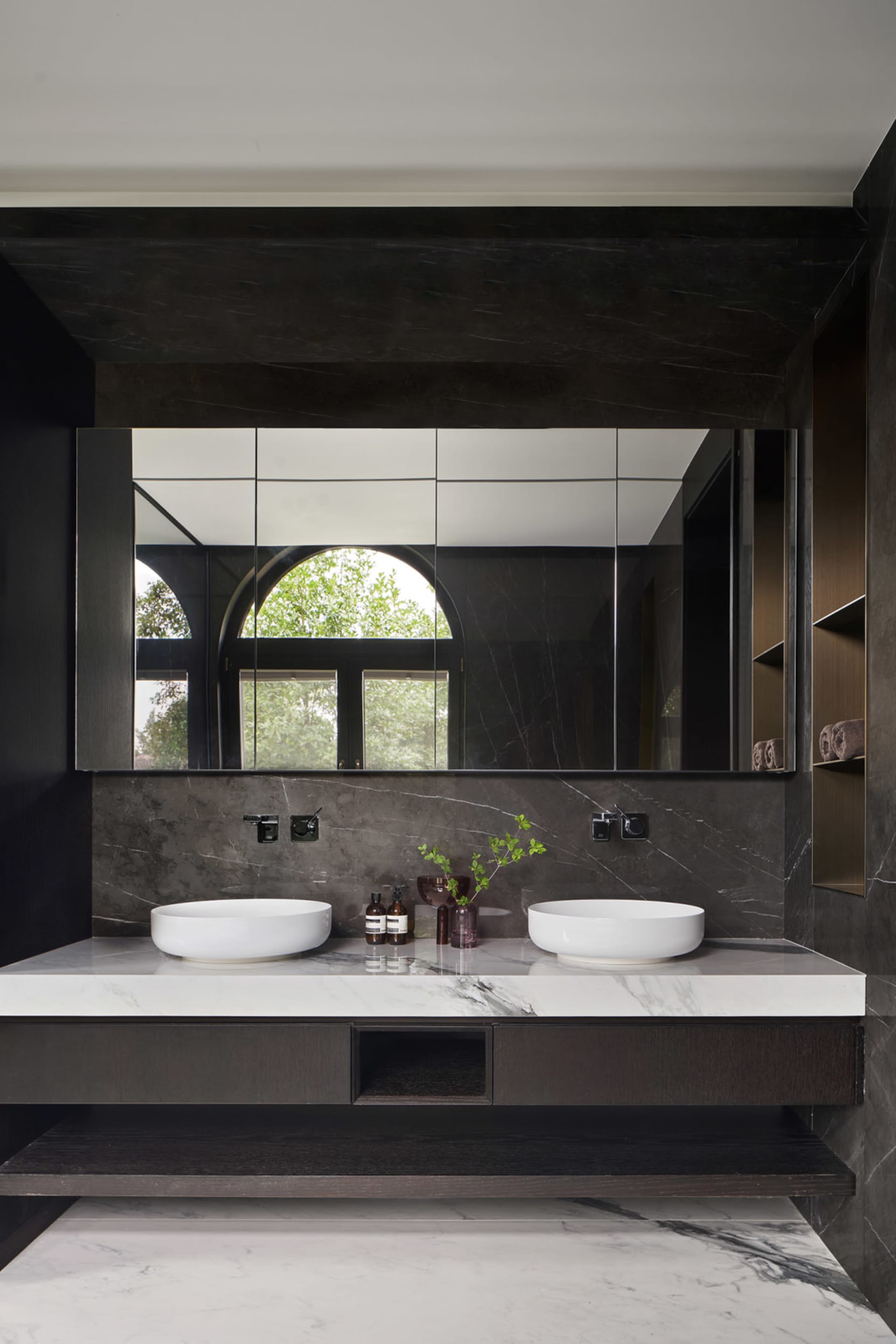A modern bathroom with a marble countertop and vanity, featuring a large mirror and a window with green trees outside.