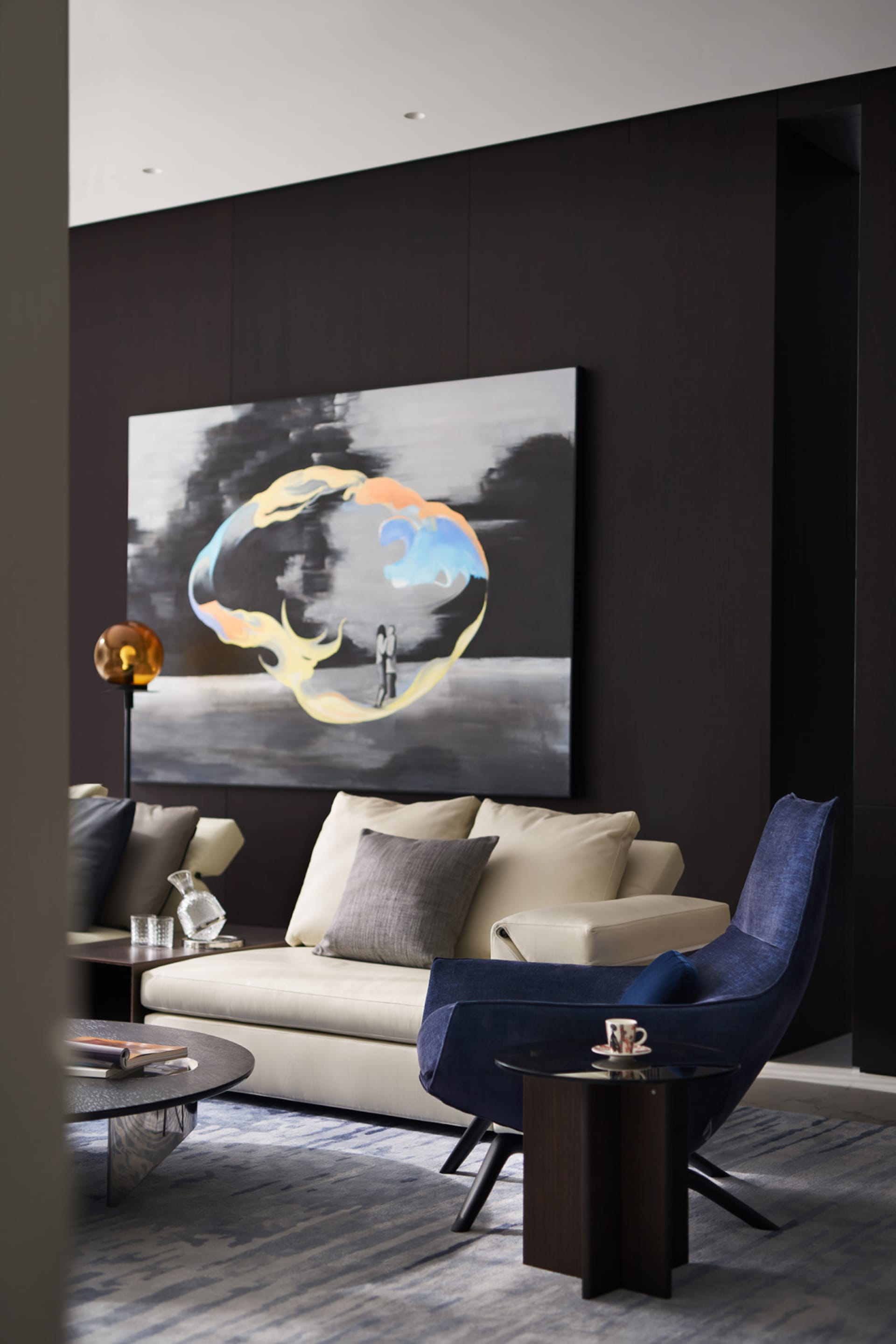 A modern living room with a blend of materials, featuring a sofa, a blue armchair, a coffee table, and a large abstract paint
