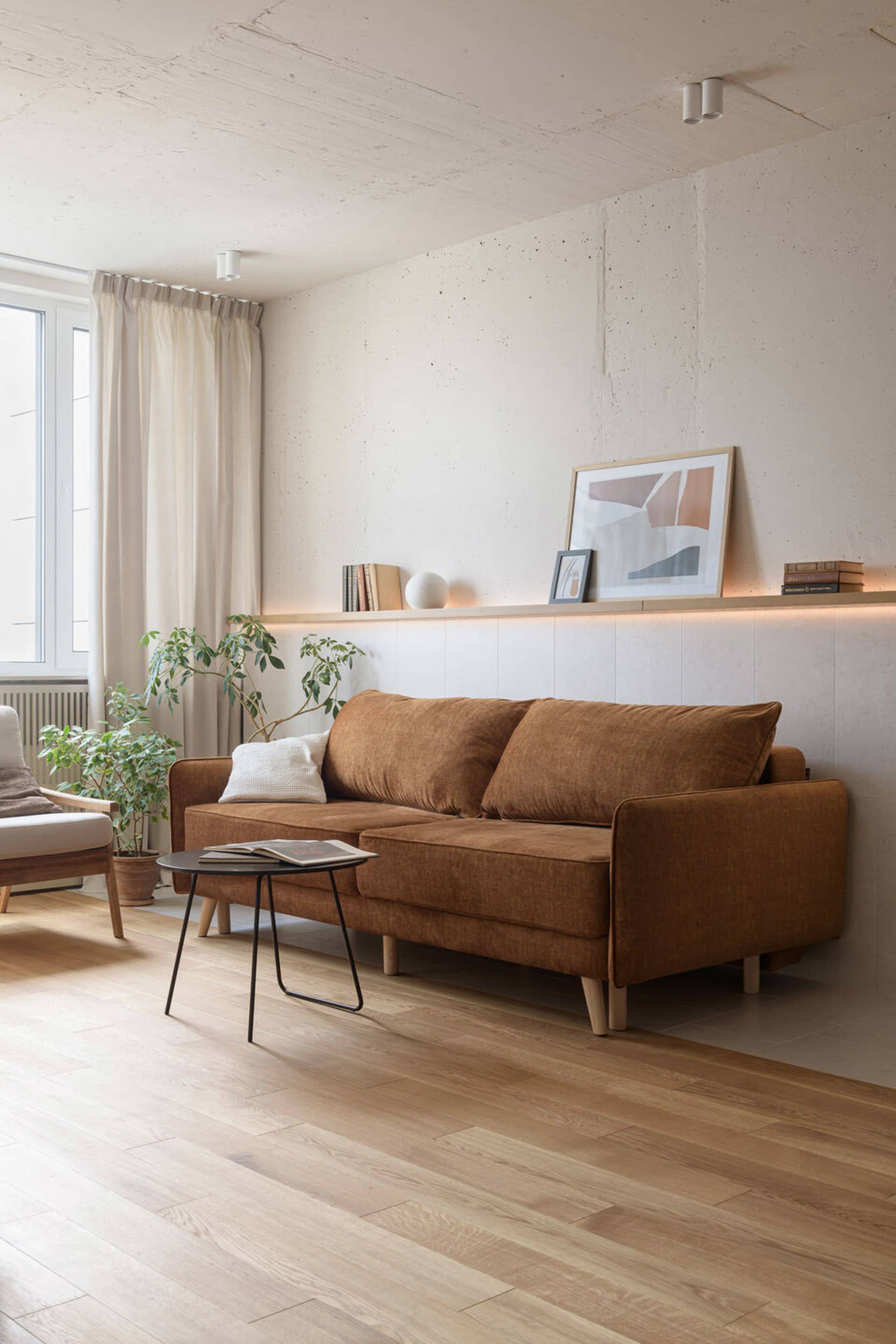 A modern living room featuring a brown sofa, wood panels, and green plants, with a picture on the wall.