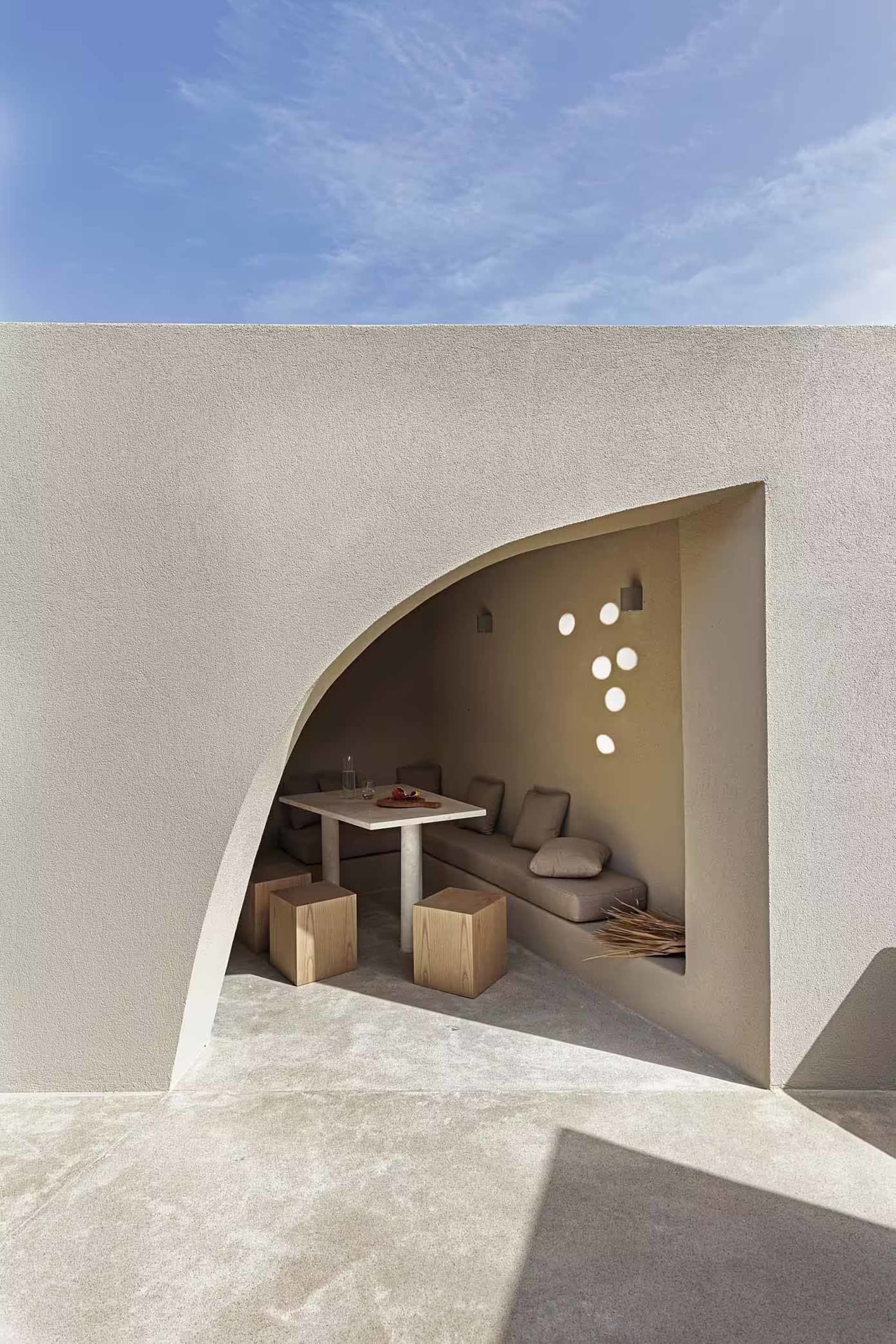 A minimalist-themed concrete outdoor living space with a curved seating area and a table setting.