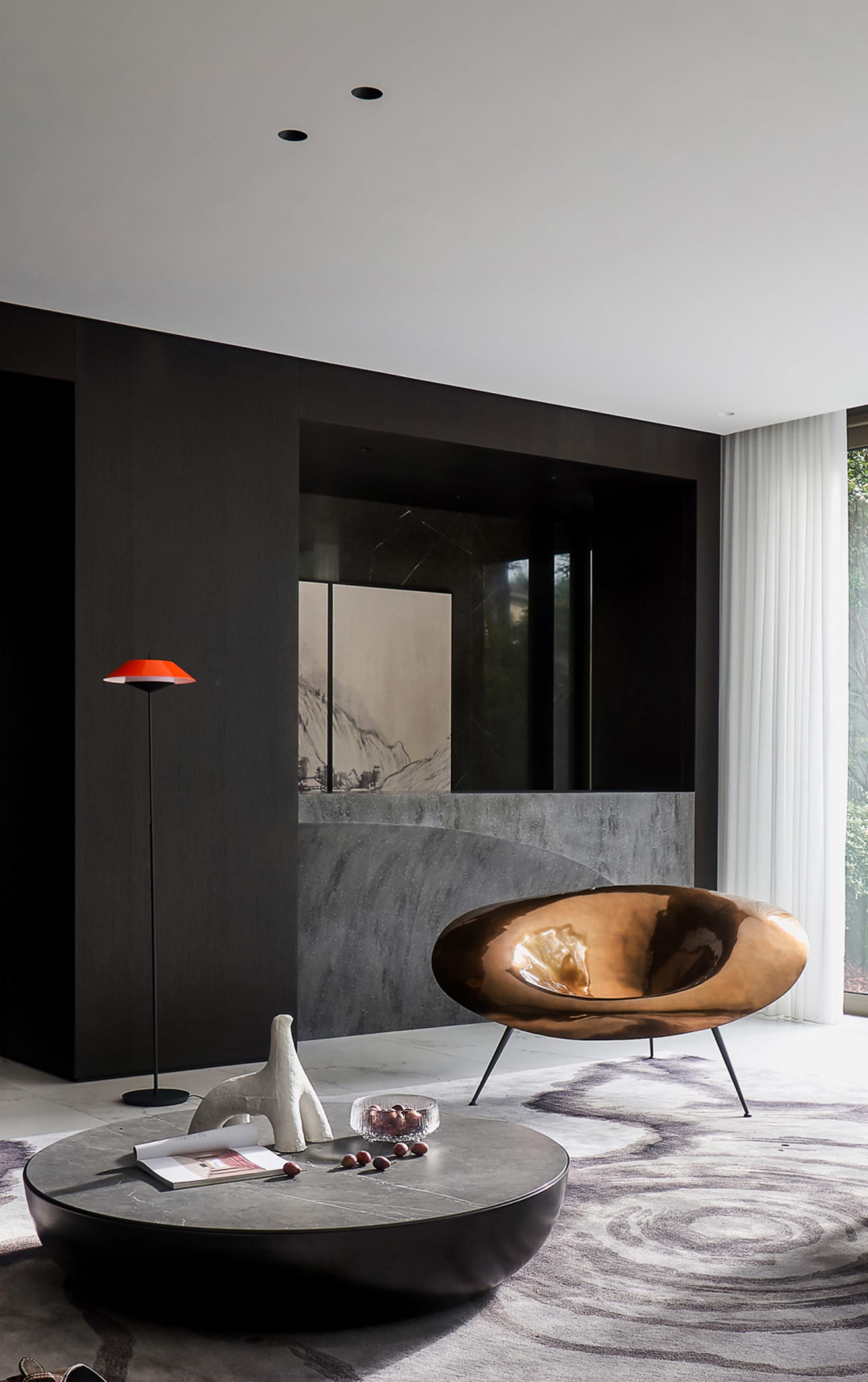 Modern minimalist living room with a bronze sculptural chair, low round table, and red floor lamp on a patterned rug with a b