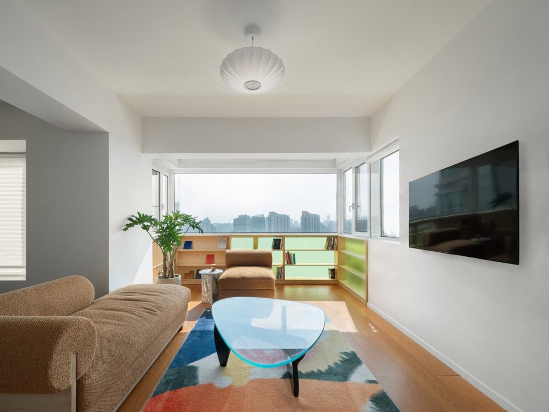 Modern living room with wooden floors, glass coffee table, fabric sofa, and floating shelves.