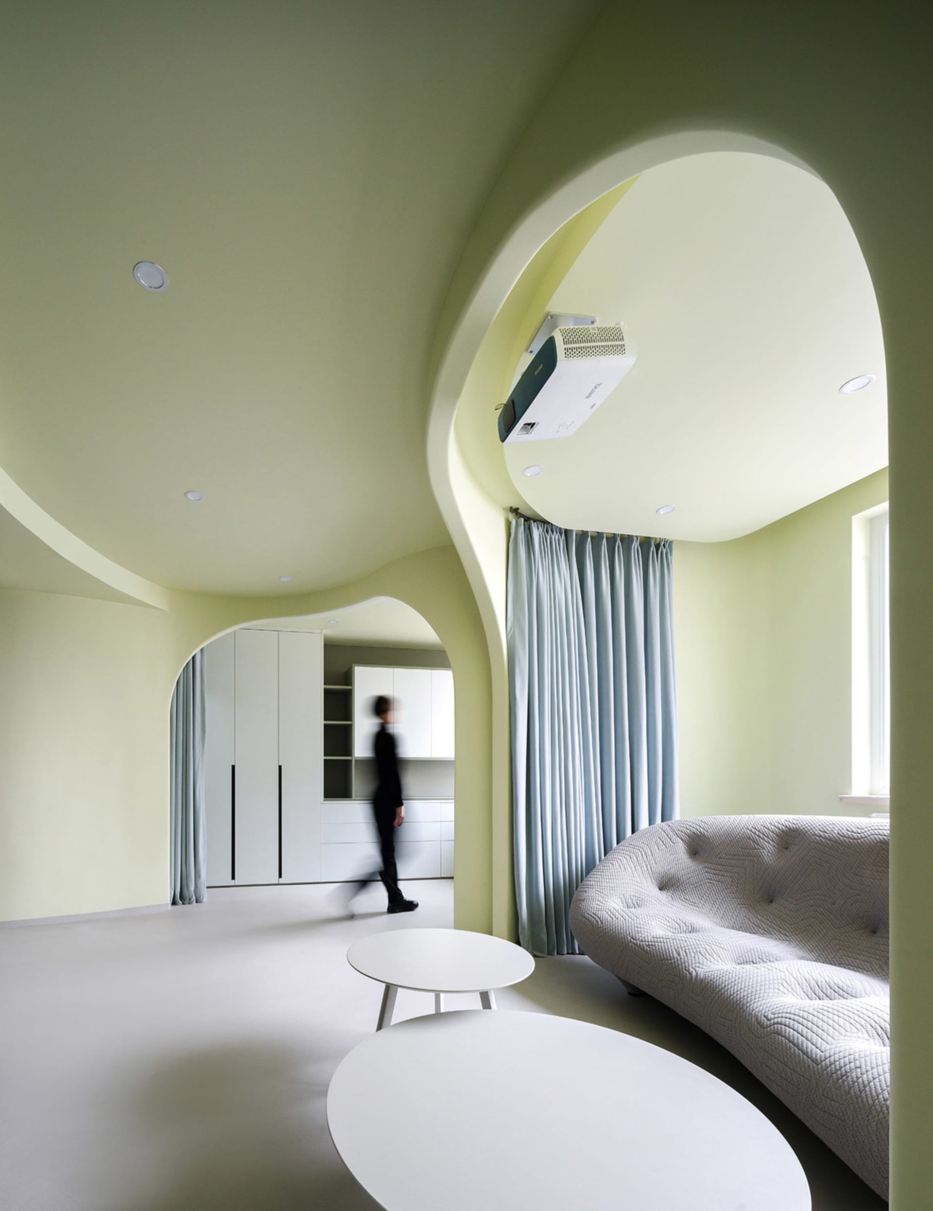 A modern white living room with a curved arch ceiling, a gray sofa, and white tables.