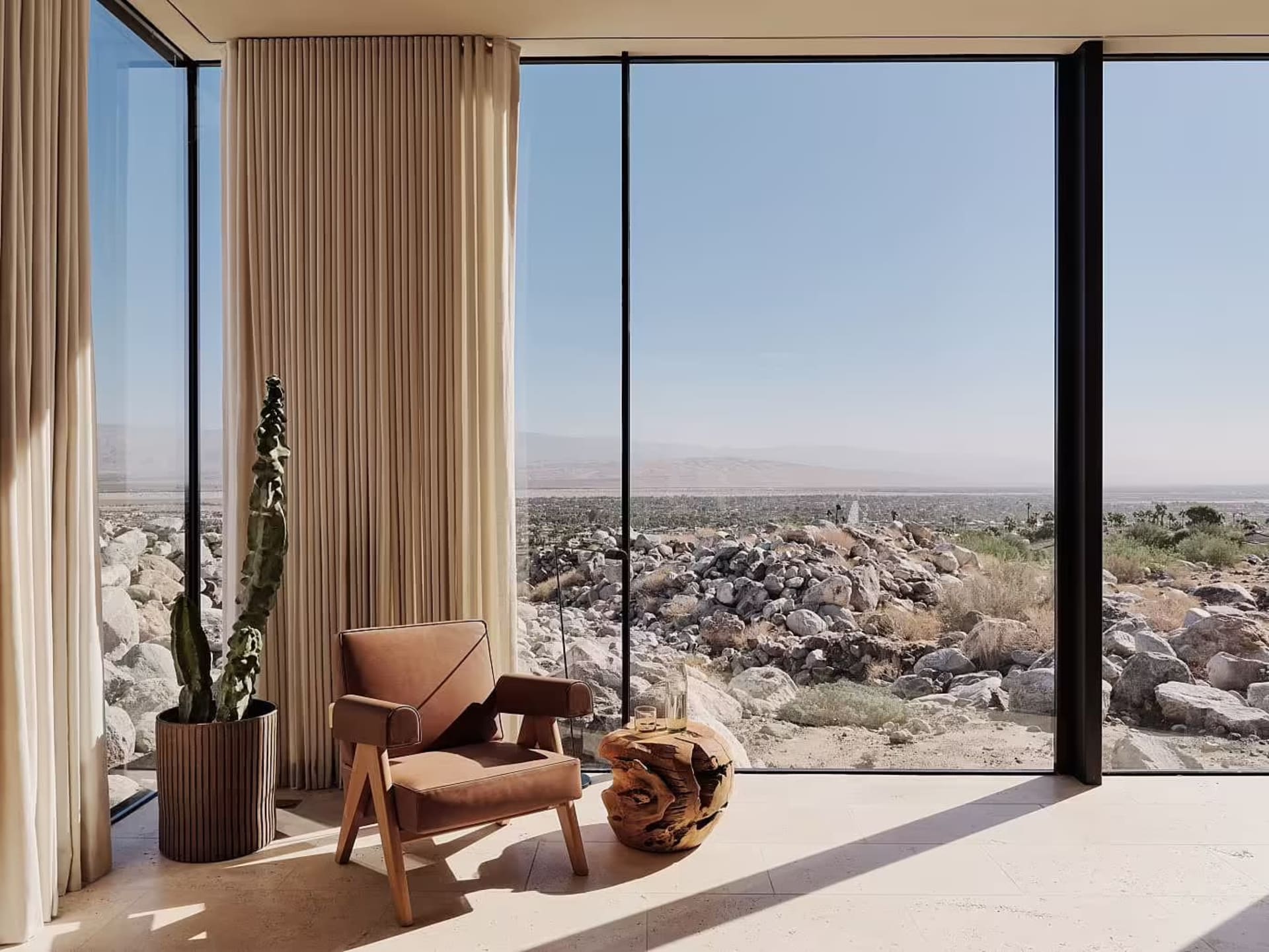 A minimalist living room with a wooden armchair and a cactus plant in a pot.
