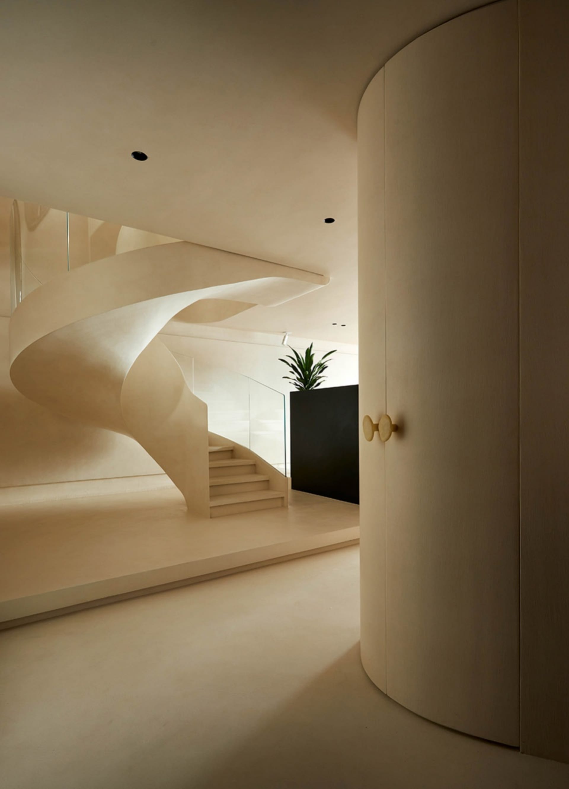 A sleek, modern staircase made of concrete with a spiral design, featuring a wall-mounted light fixture and a plant in the ba