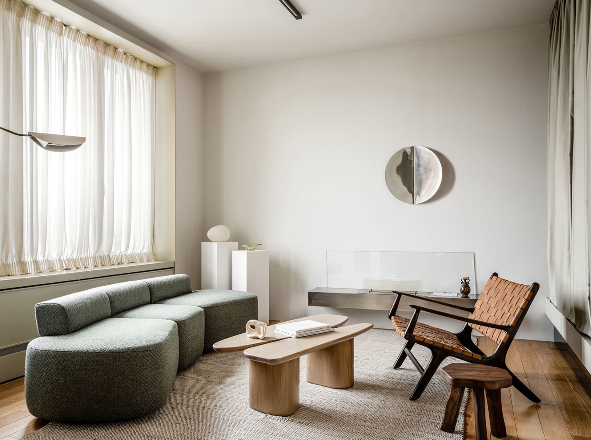 A modern minimalist living room featuring a gray upholstered sofa, wooden side tables, and glass wall decor.