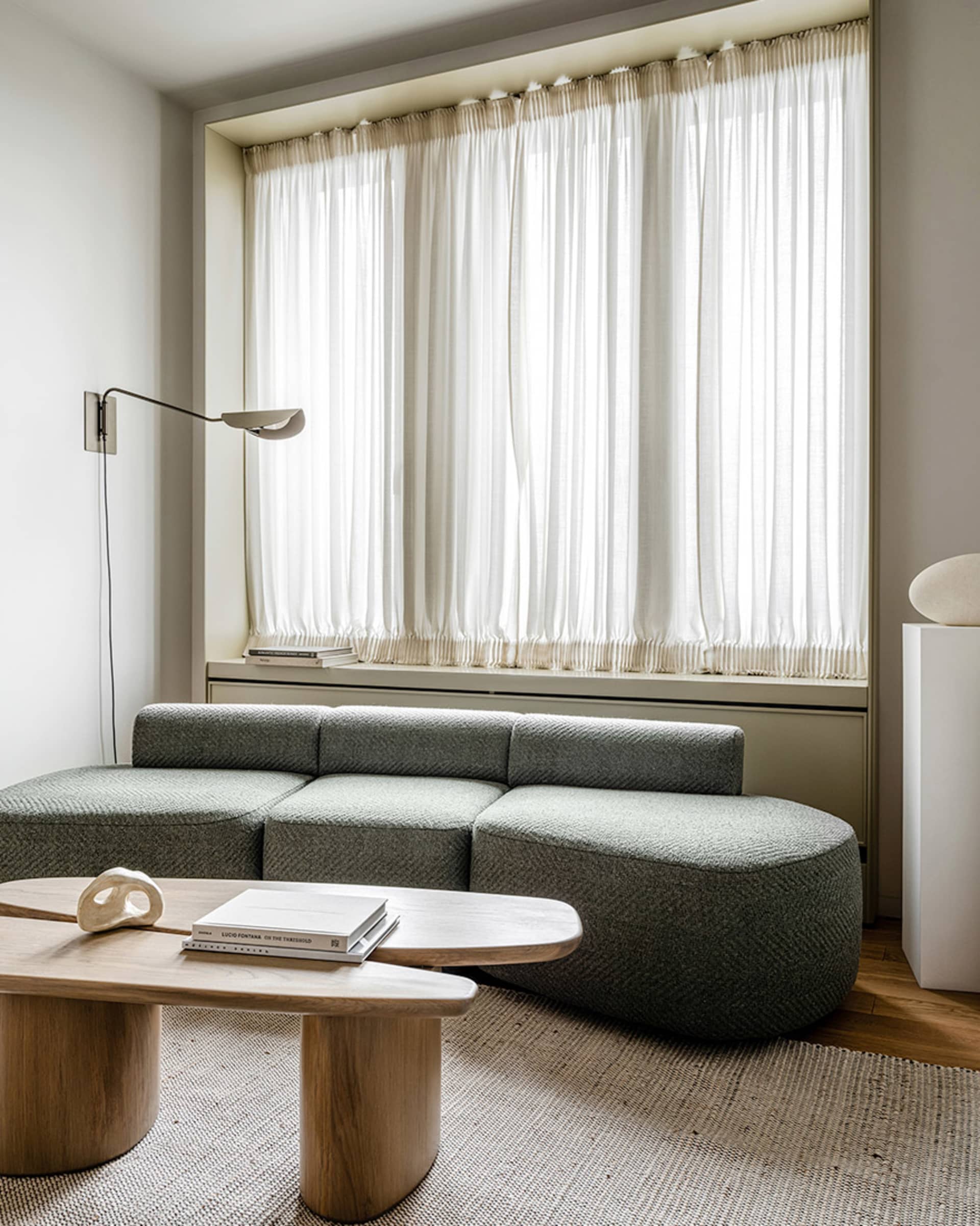 Modern living room with a green sofa, wooden coffee table, and large window with sheer curtains.