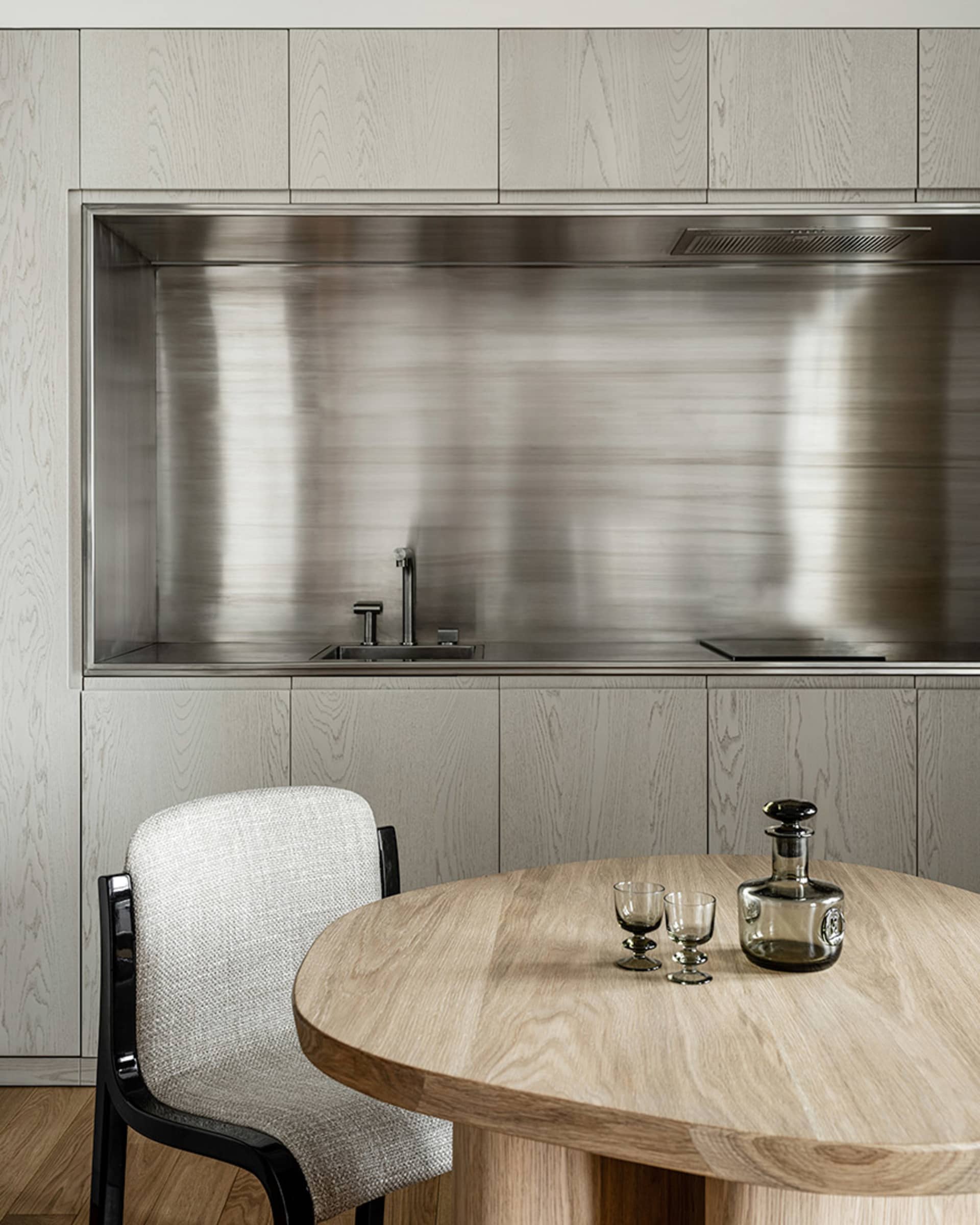 A minimalist modern kitchen with metallic finishes and a round wooden table.