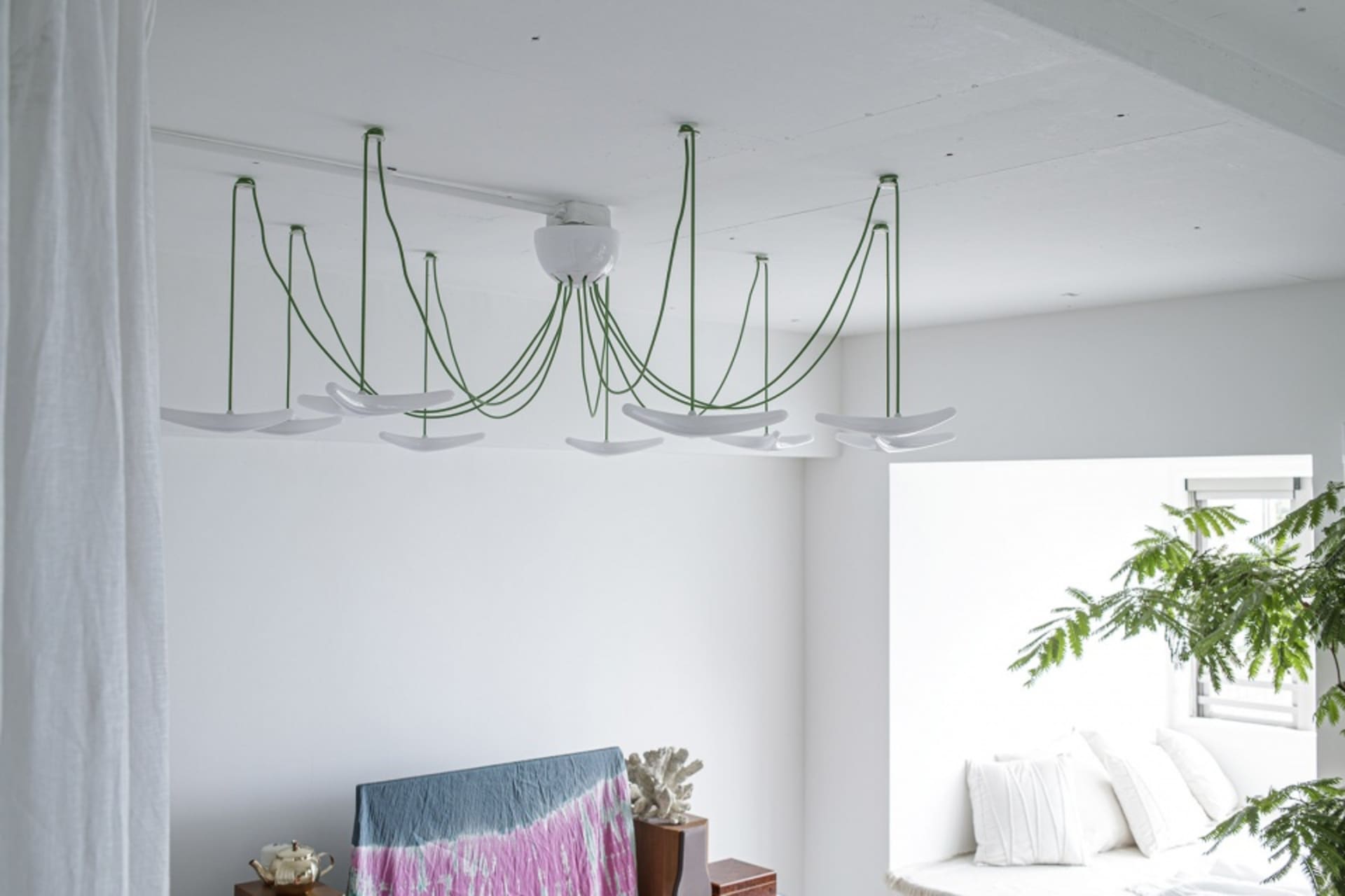 A modern, industrial-style living room with exposed concrete ceiling, a chandelier with green, hanging cables, and a white so