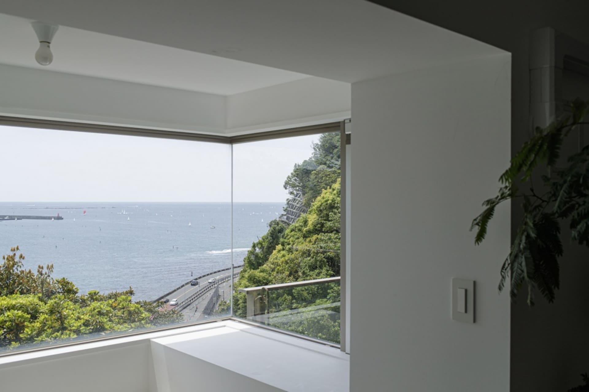 現代住宅窗戶提供玻璃視野，眺望海洋與茂密綠意。