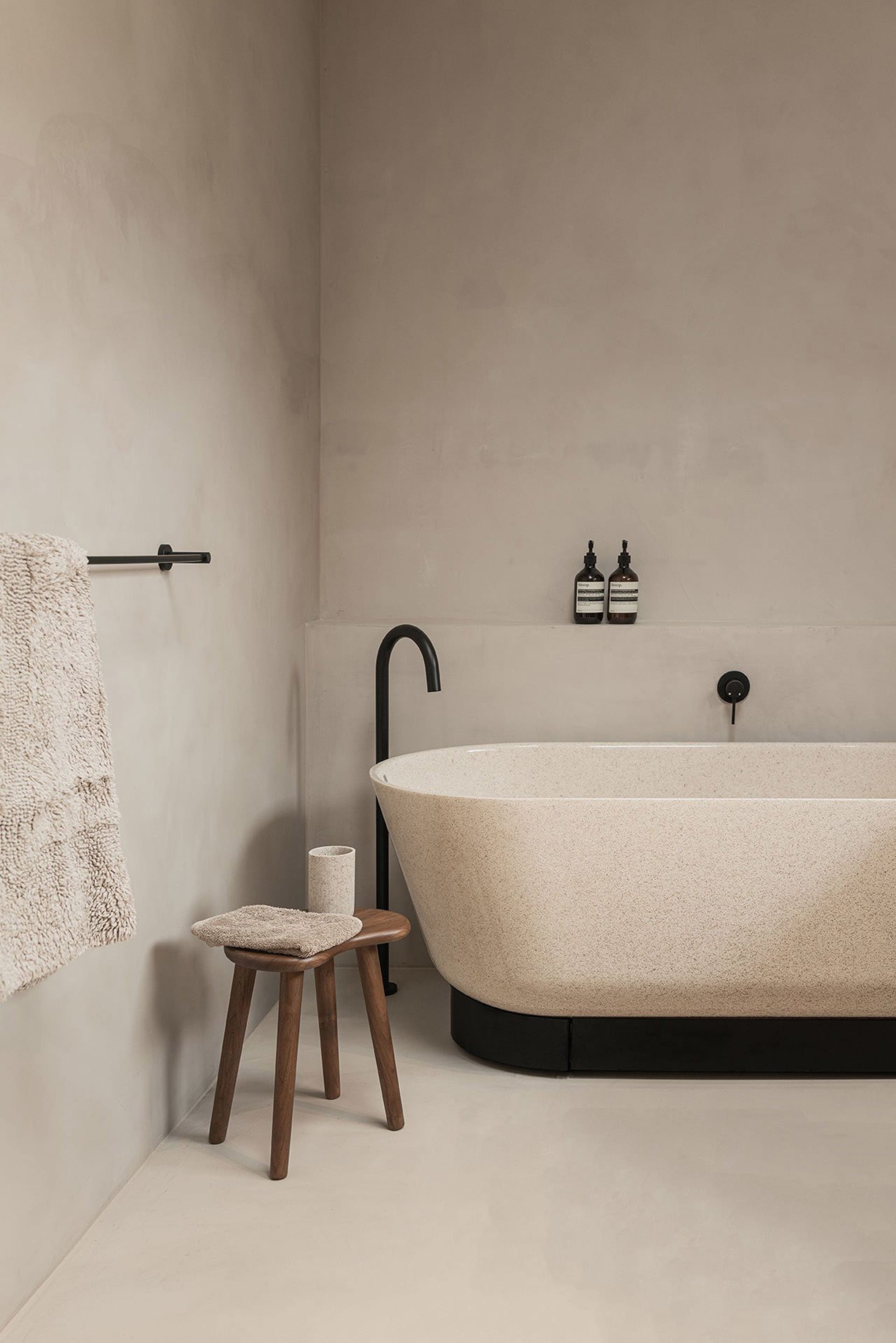 A minimalist bathroom featuring a terrazzo bathtub and stool.