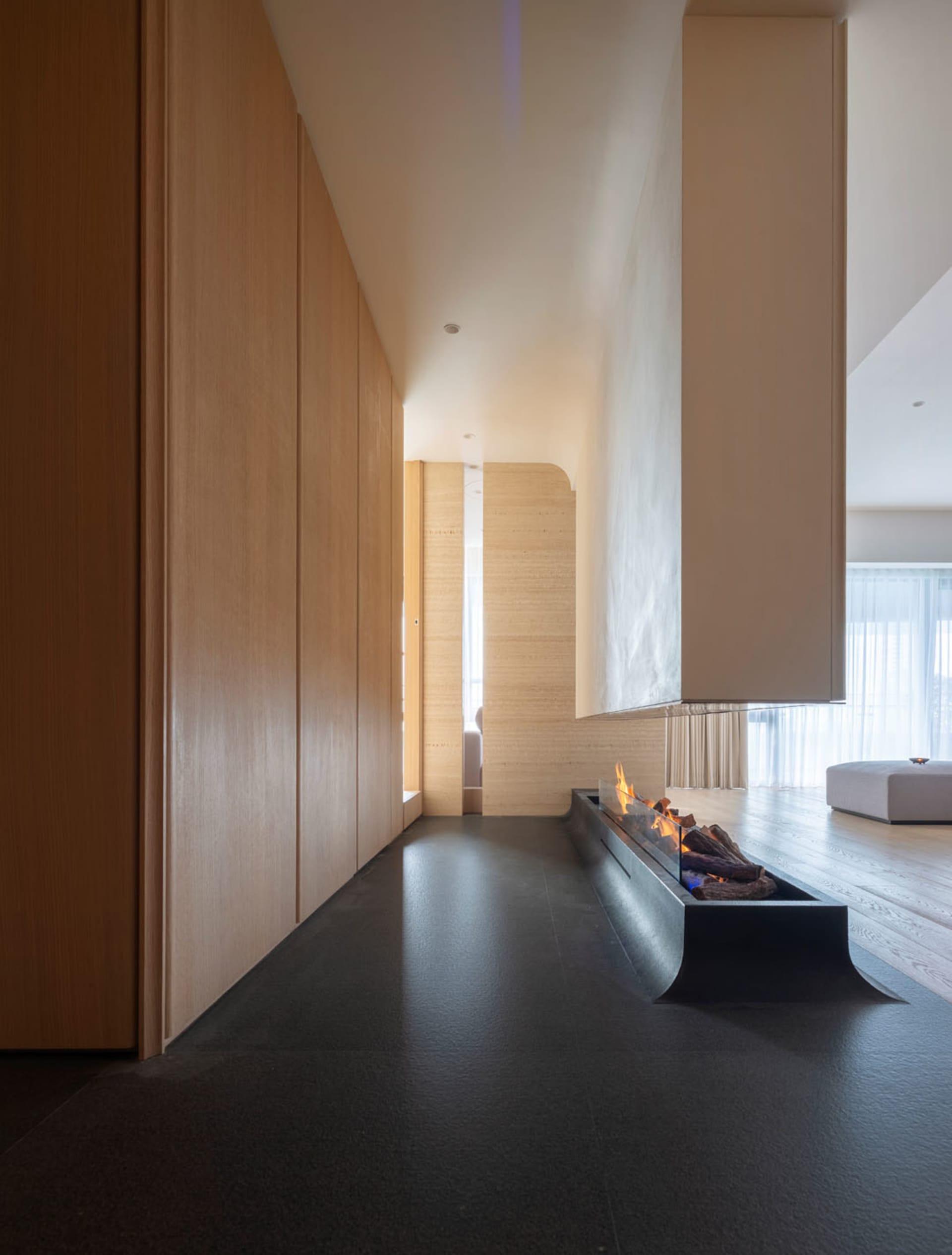 Modern living room featuring wood cabinets, a concrete floor, and clay walls, with a modern fireplace.
