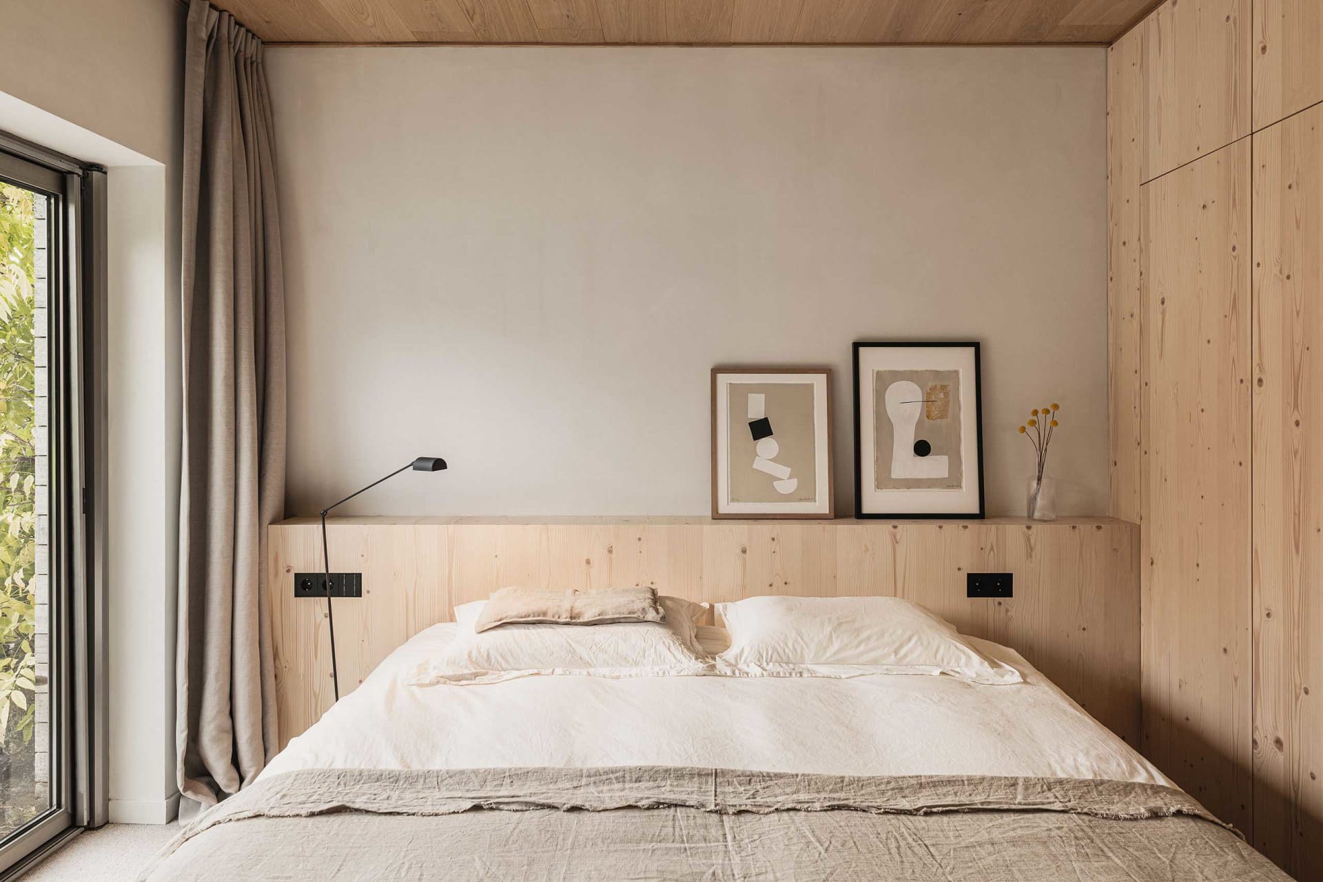 A modern minimalist bedroom with a wooden headboard and abstract art.