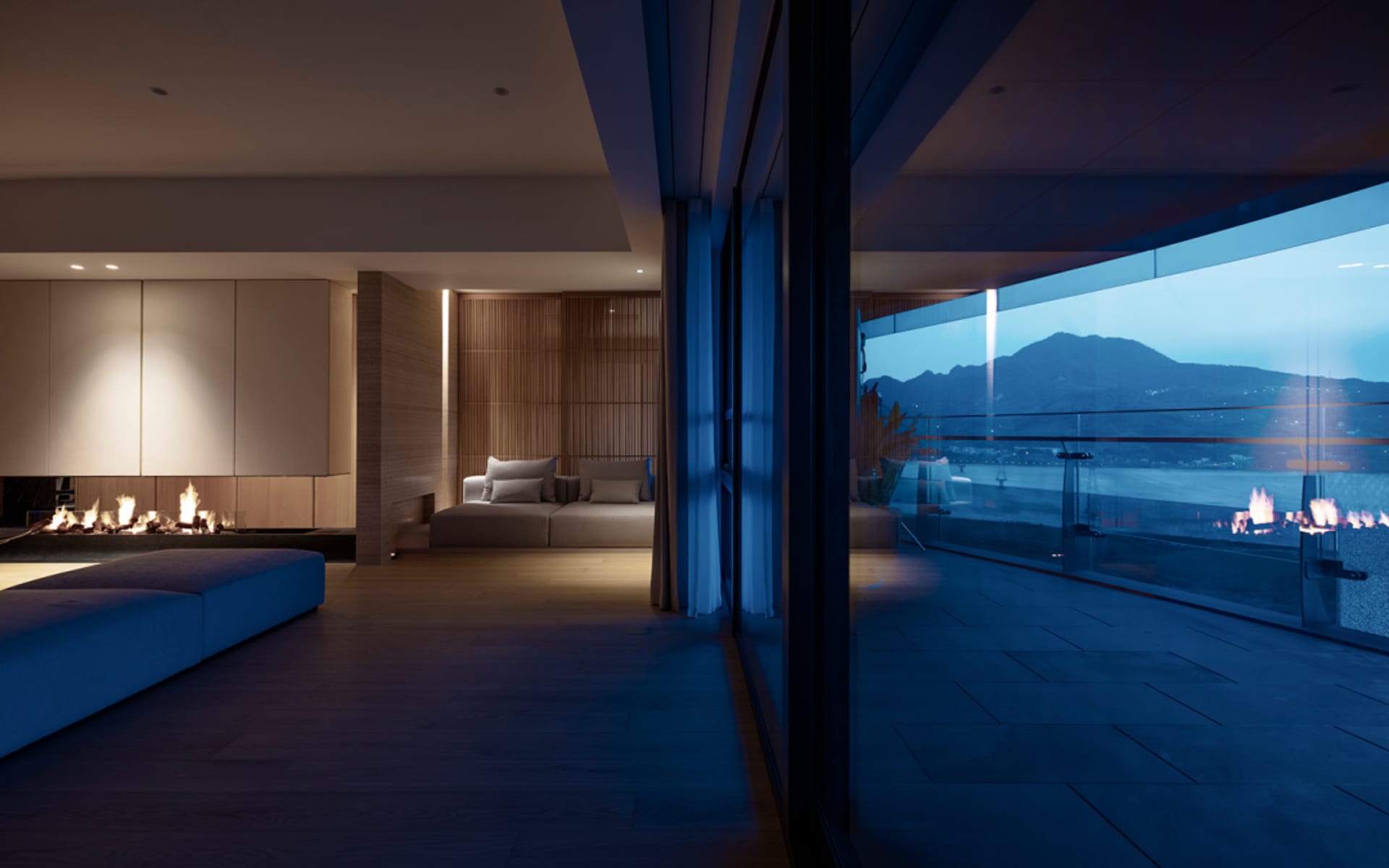 Modern living room featuring wooden flooring, contemporary furniture, and a view of mountains through large windows.