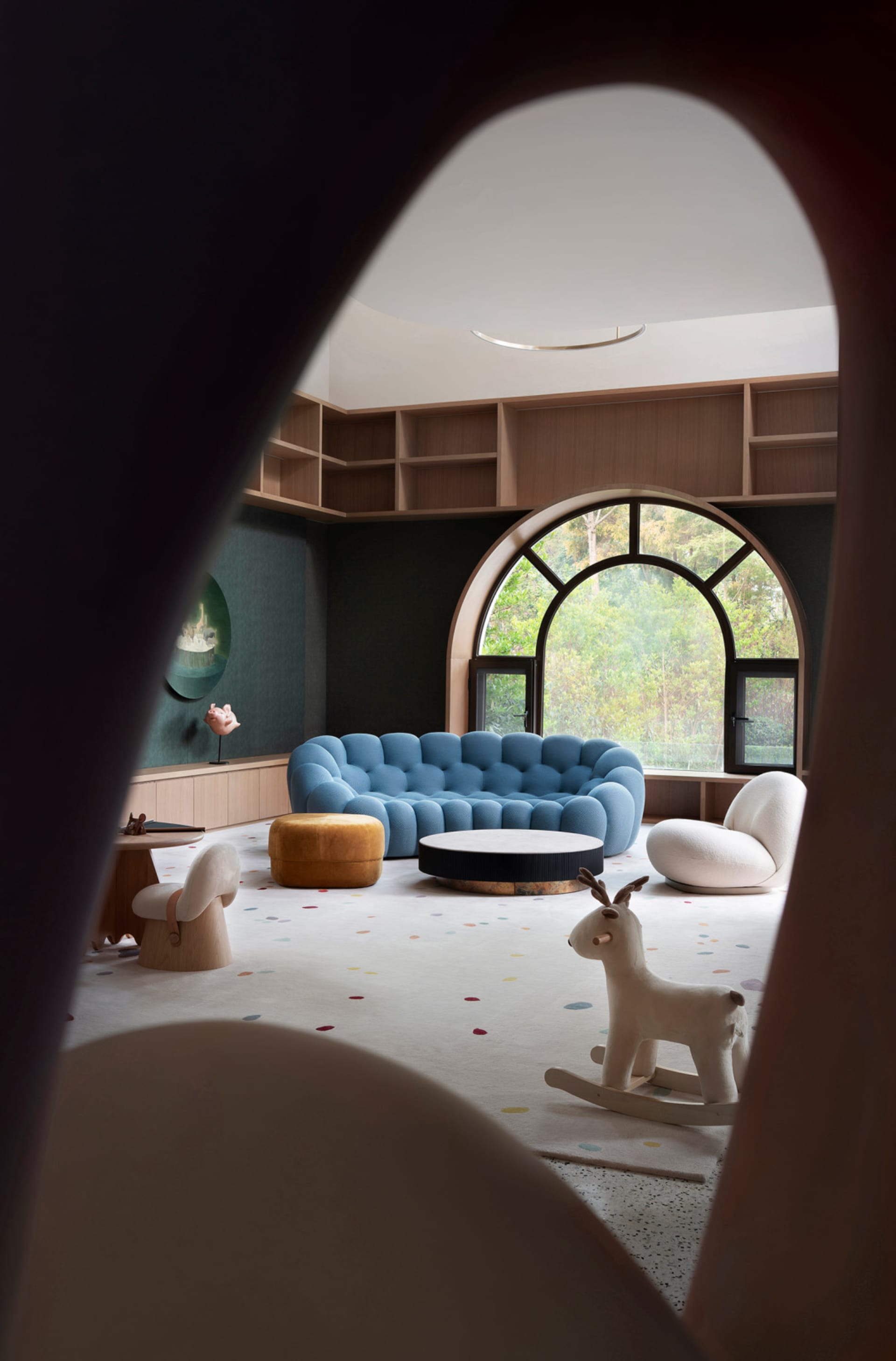 A modern playroom with a blue sofa, white rocking horse, and colorful floor