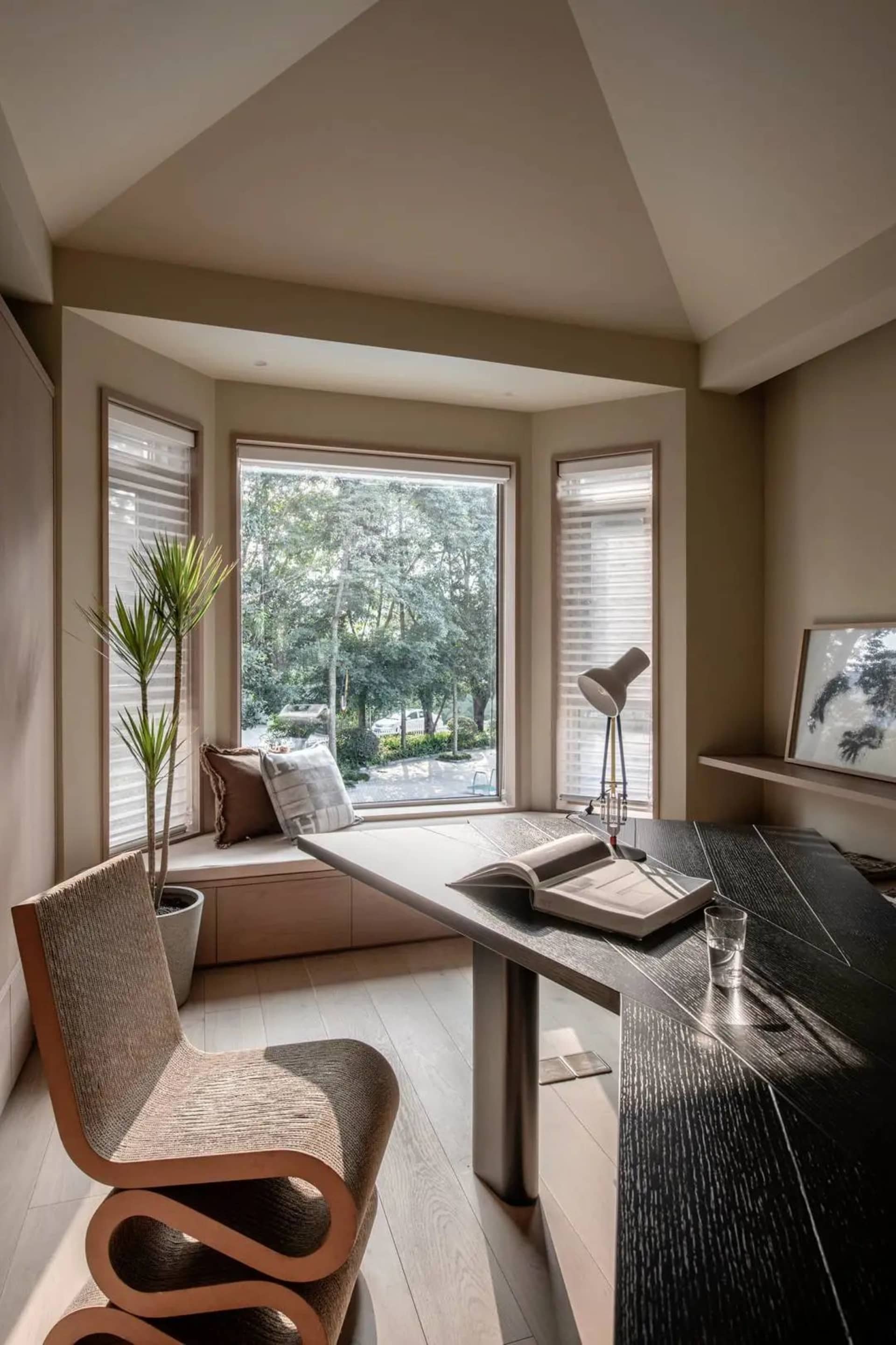A modern minimalist home office space featuring a sleek wooden desk, glass windows, and a comfortable seating area with natur
