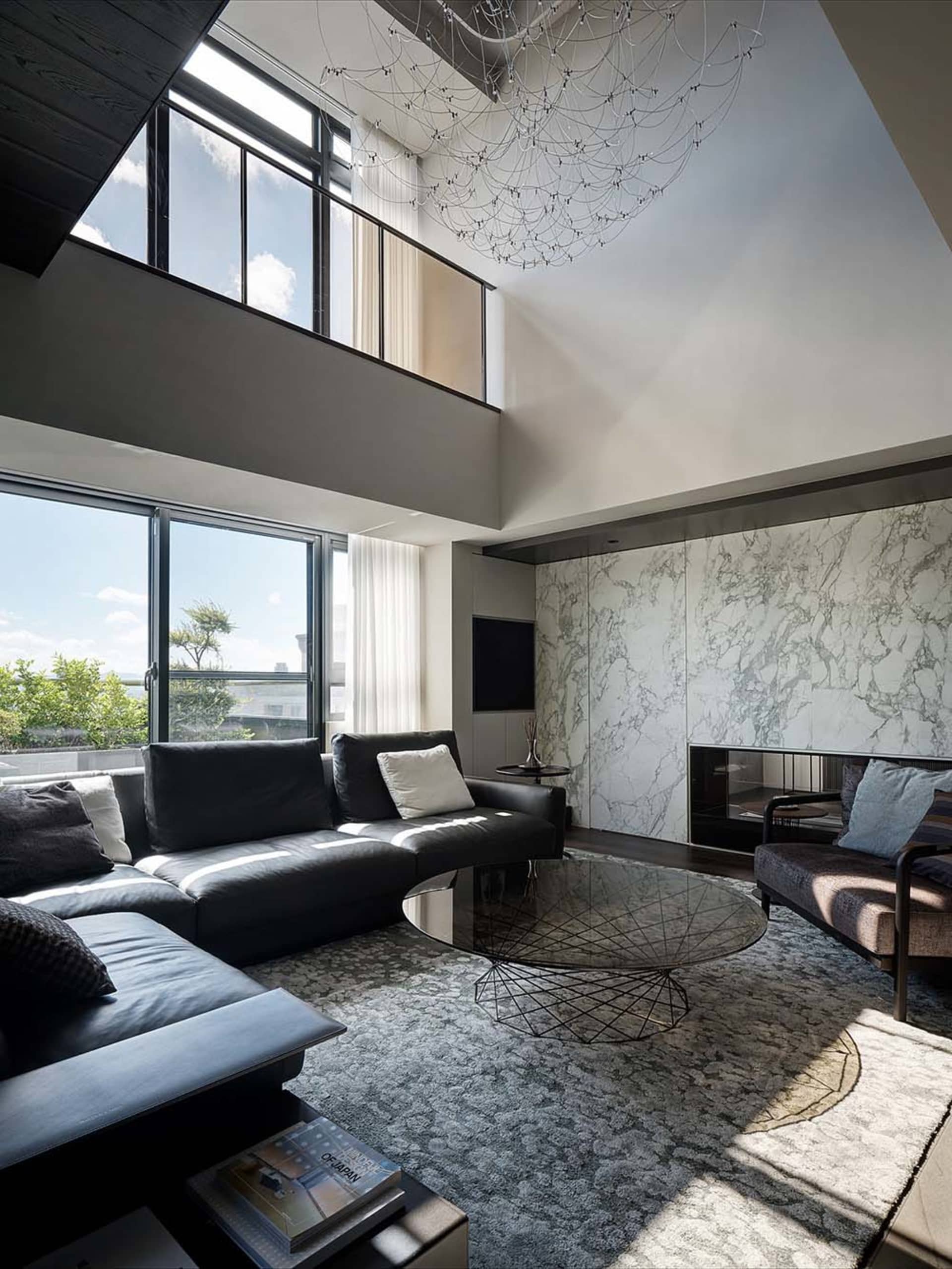 A modern living room featuring marble finishes and glass elements, with large windows and a high ceiling.