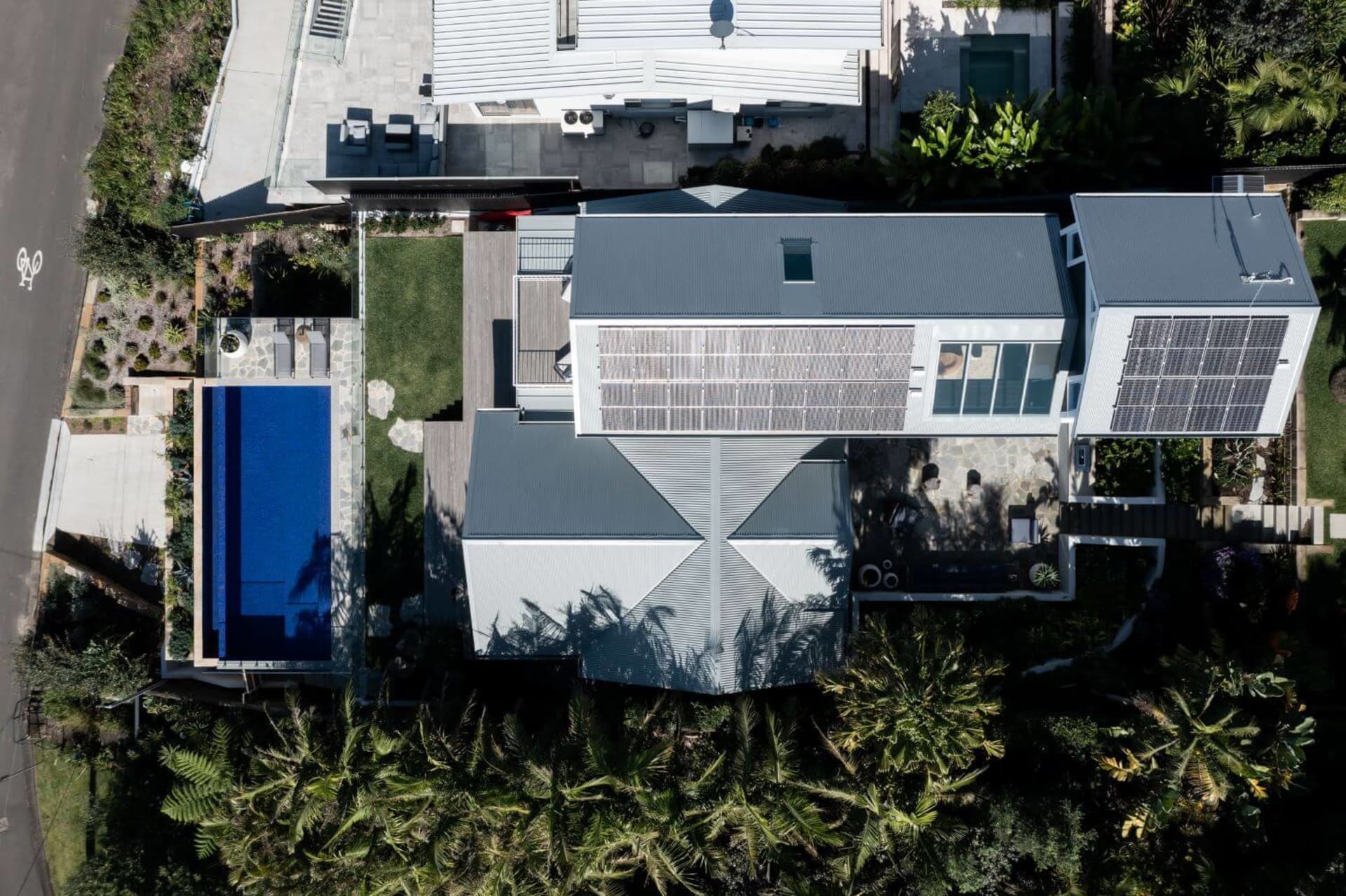 A modern residential exterior featuring metal, glass, and concrete materials with a landscaped garden.