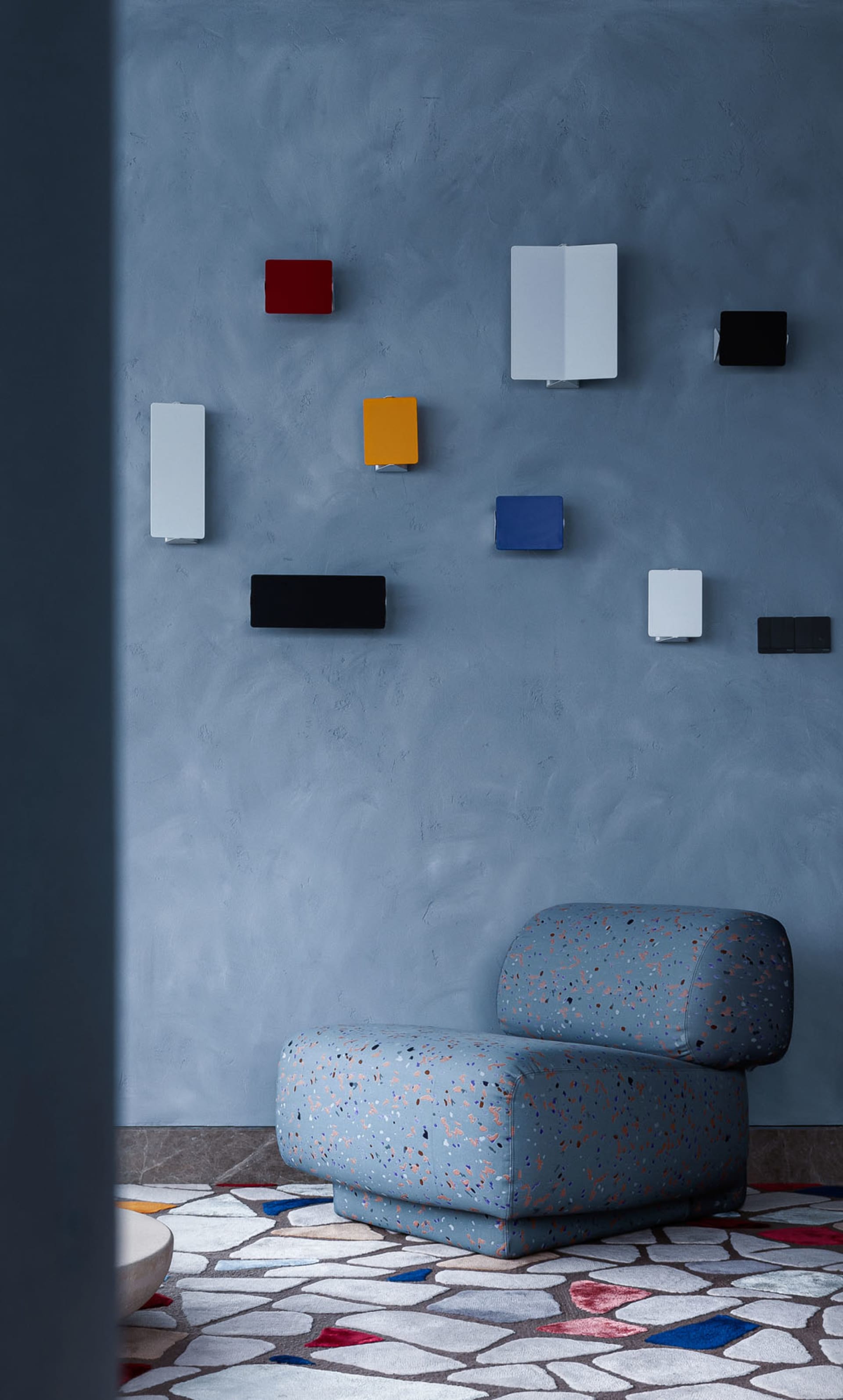 A minimalist living room with terrazzo flooring, featuring a modern, comfortable chair and colorful wall art.