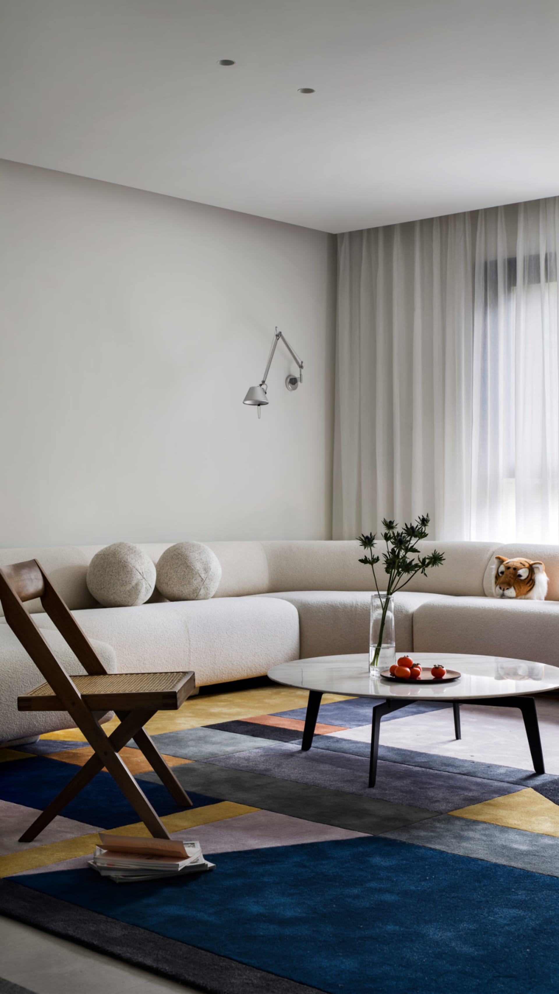 A modern interior living room with a large, curved sofa upholstered in white fabric, a wooden folding chair, a round coffee t