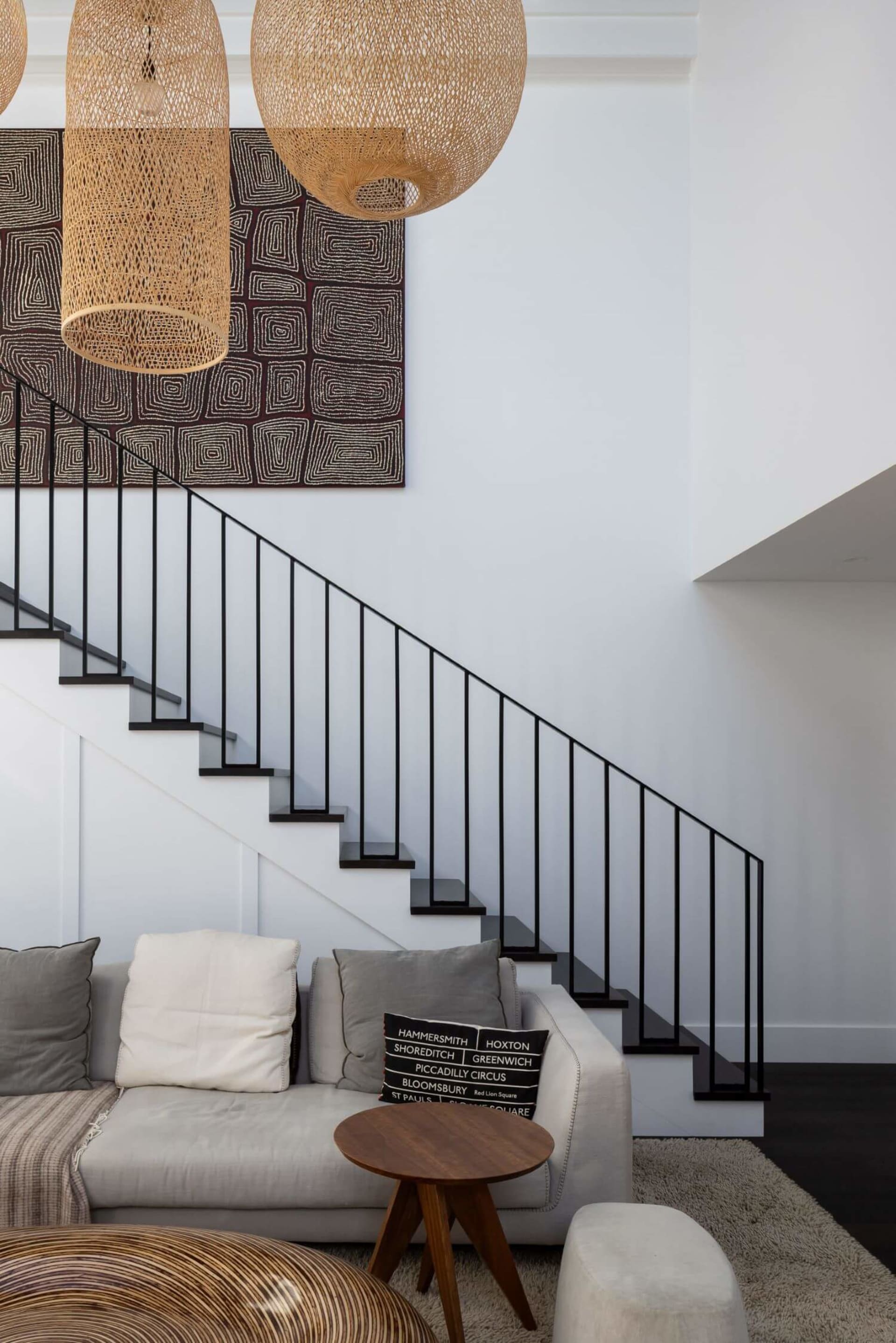Modern living room featuring a contemporary staircase with black metal railing, a woven pendant light, a white sectional sofa