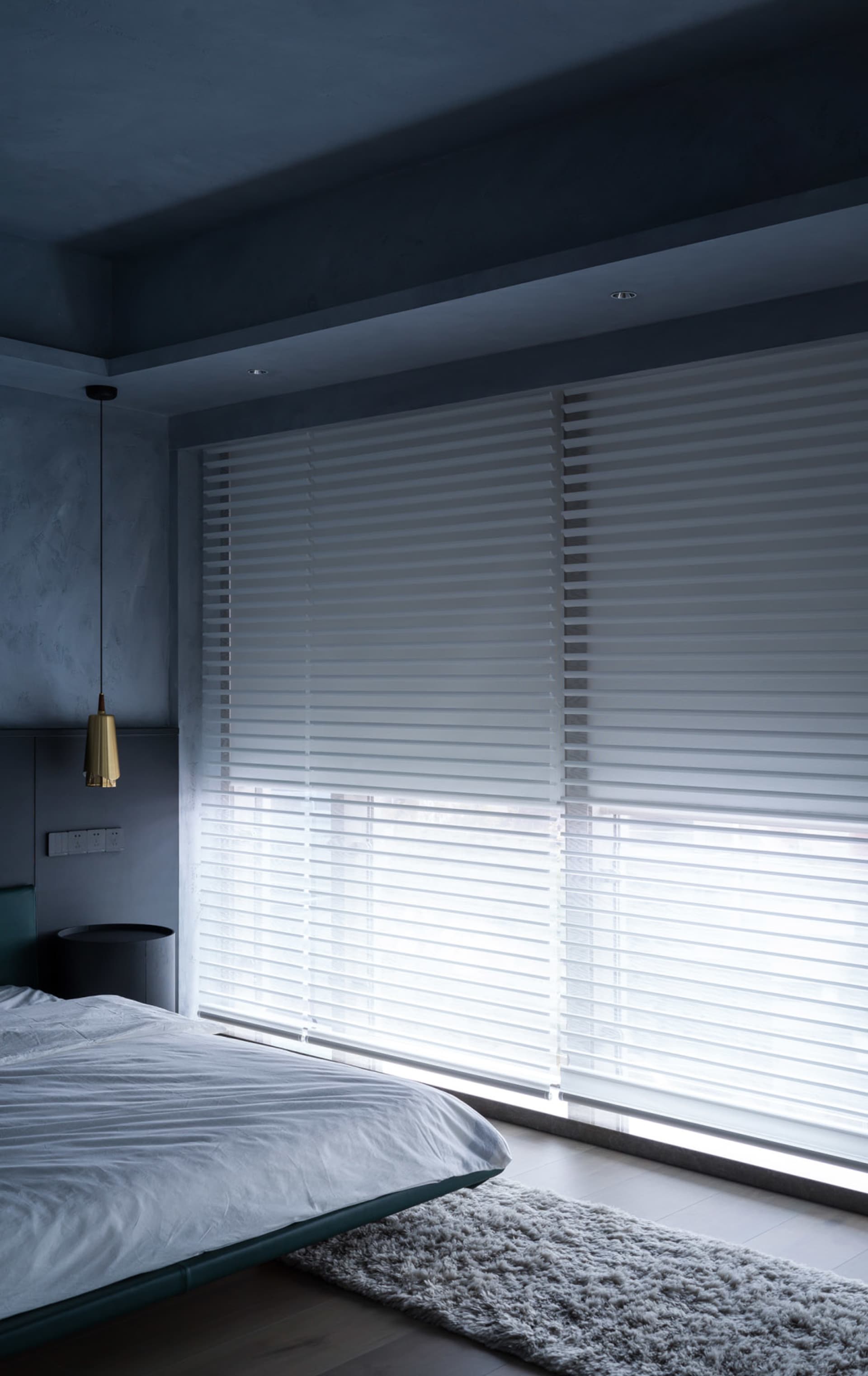 A modern minimalist bedroom with silk blinds, a cozy rug, and a sleek bed.