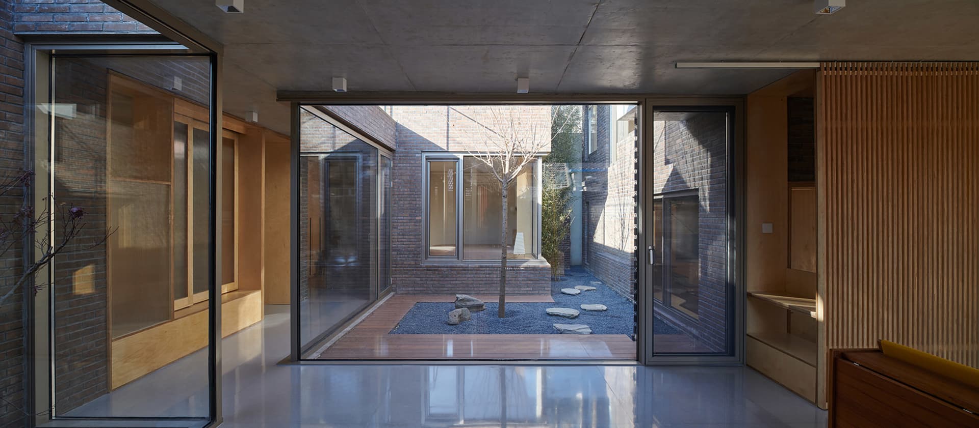 Modern residential interior featuring glass windows, brick walls, and concrete floors.