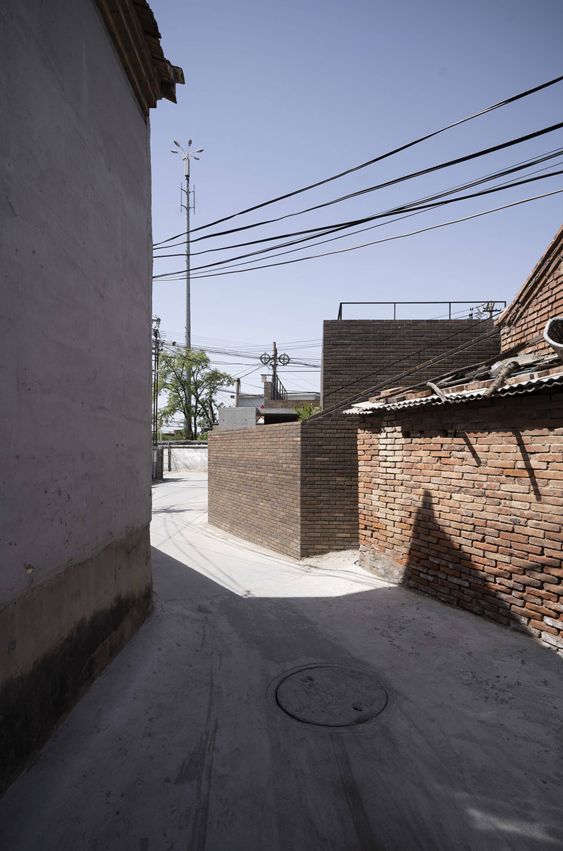 A narrow urban alley lined with brick buildings, featuring overhead power lines and a concrete pathway.